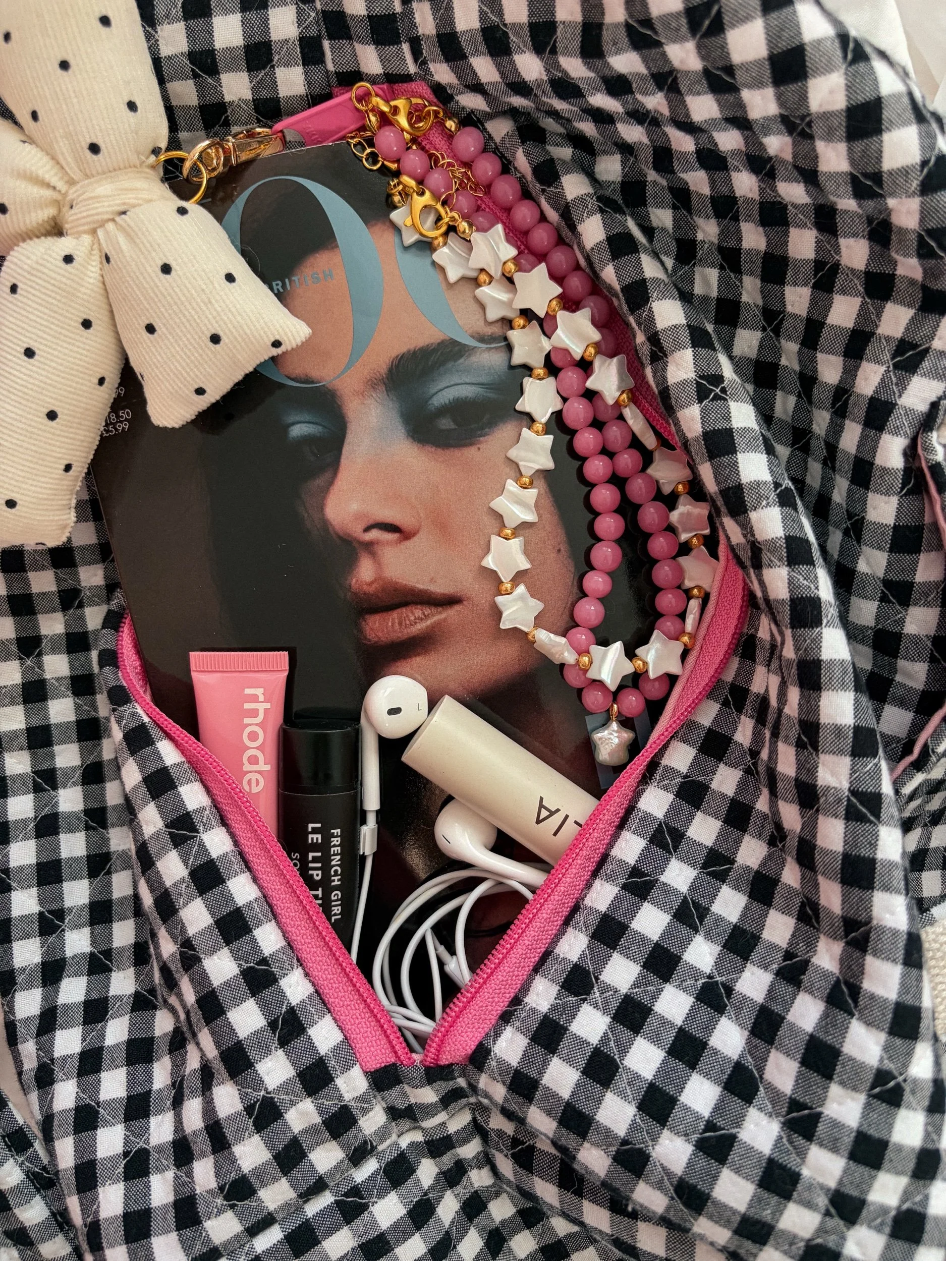 Pink beaded necklaces and a white star bead necklace styled in a black and white gingham bag with a pink zipper