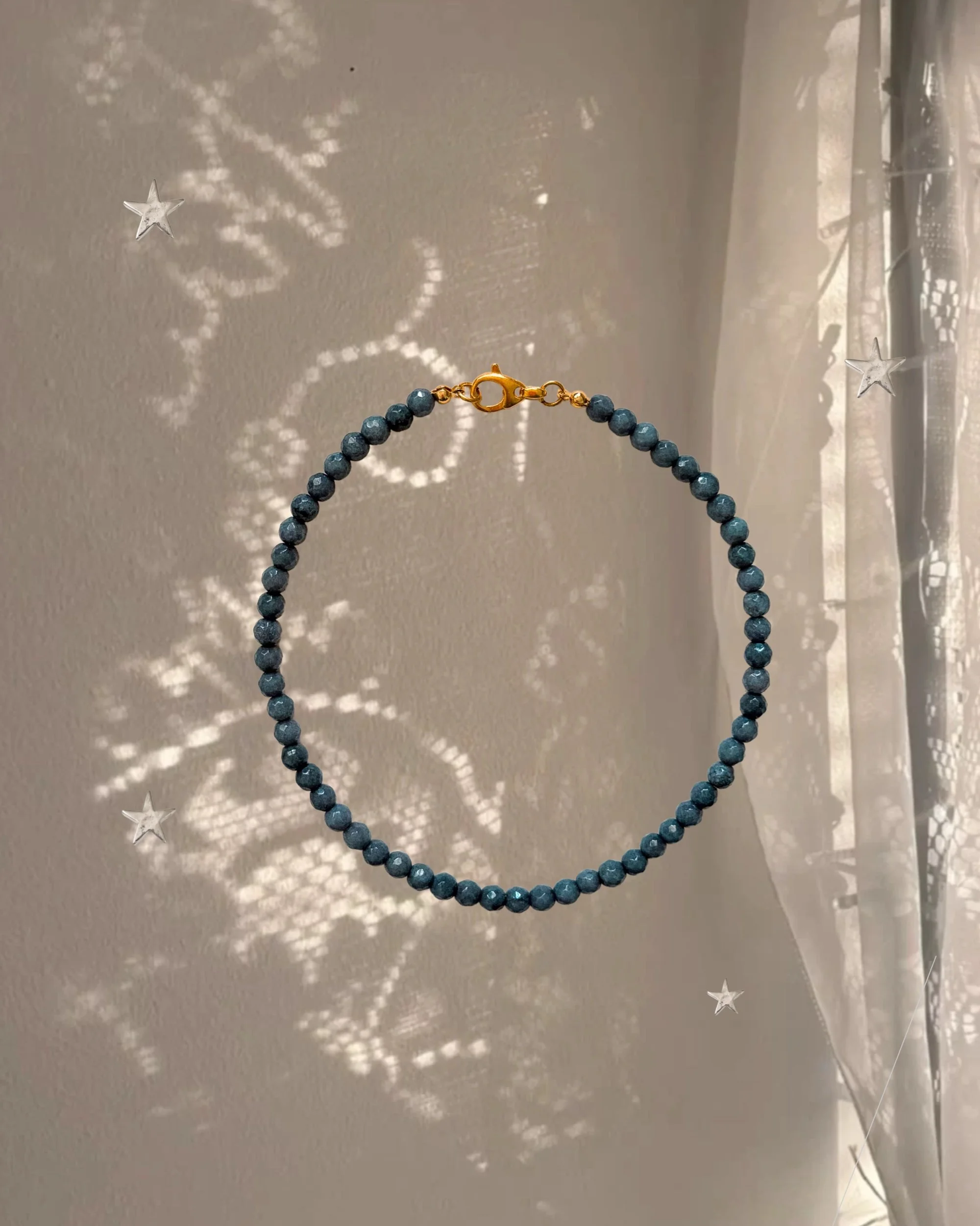 Stormy Gray beaded necklace with gold clasp against a sheer curtain with sparkly star-shaped light