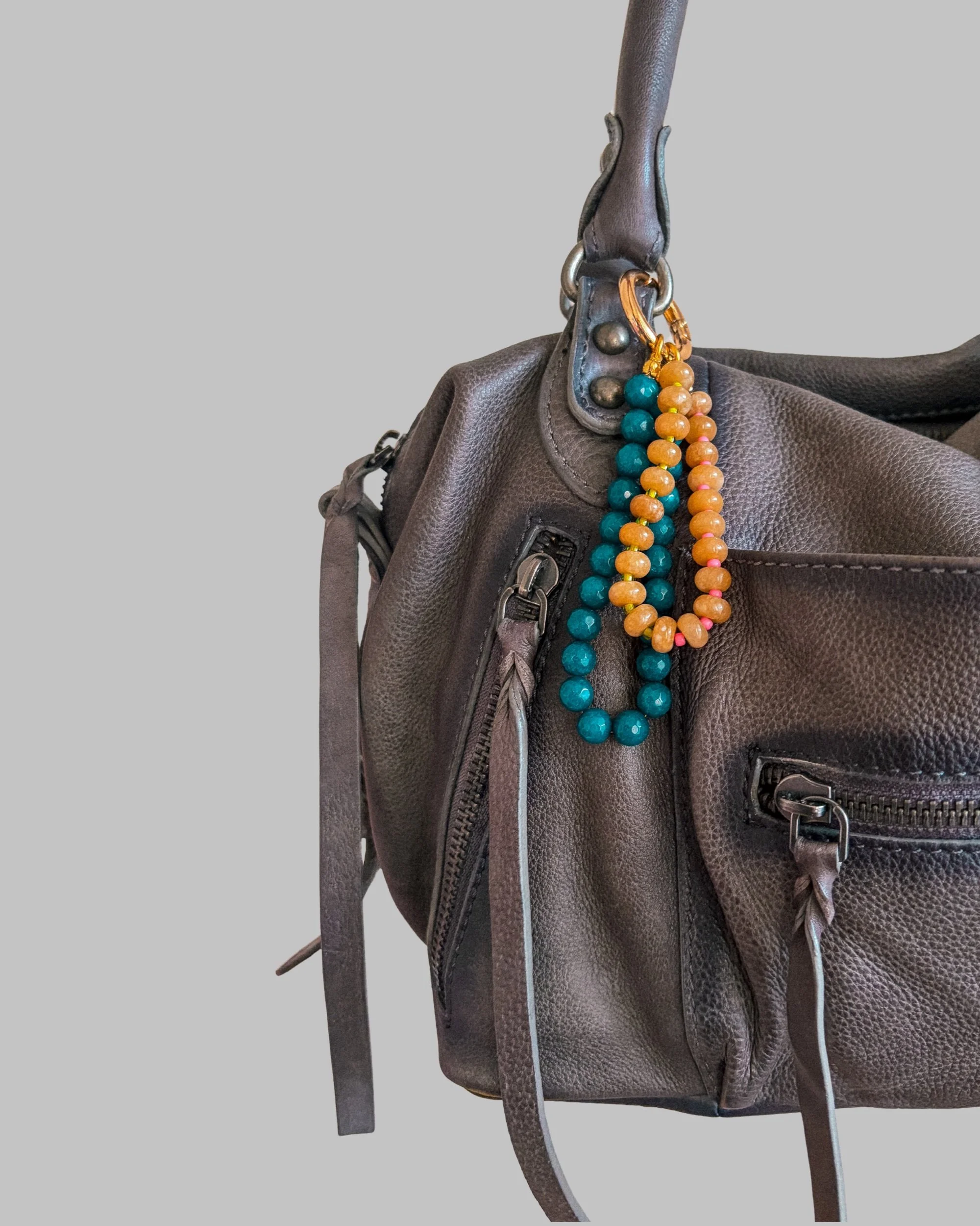 Wild Teal Beaded Bag Charm clipped to a gray leather handbag against a plain gray background