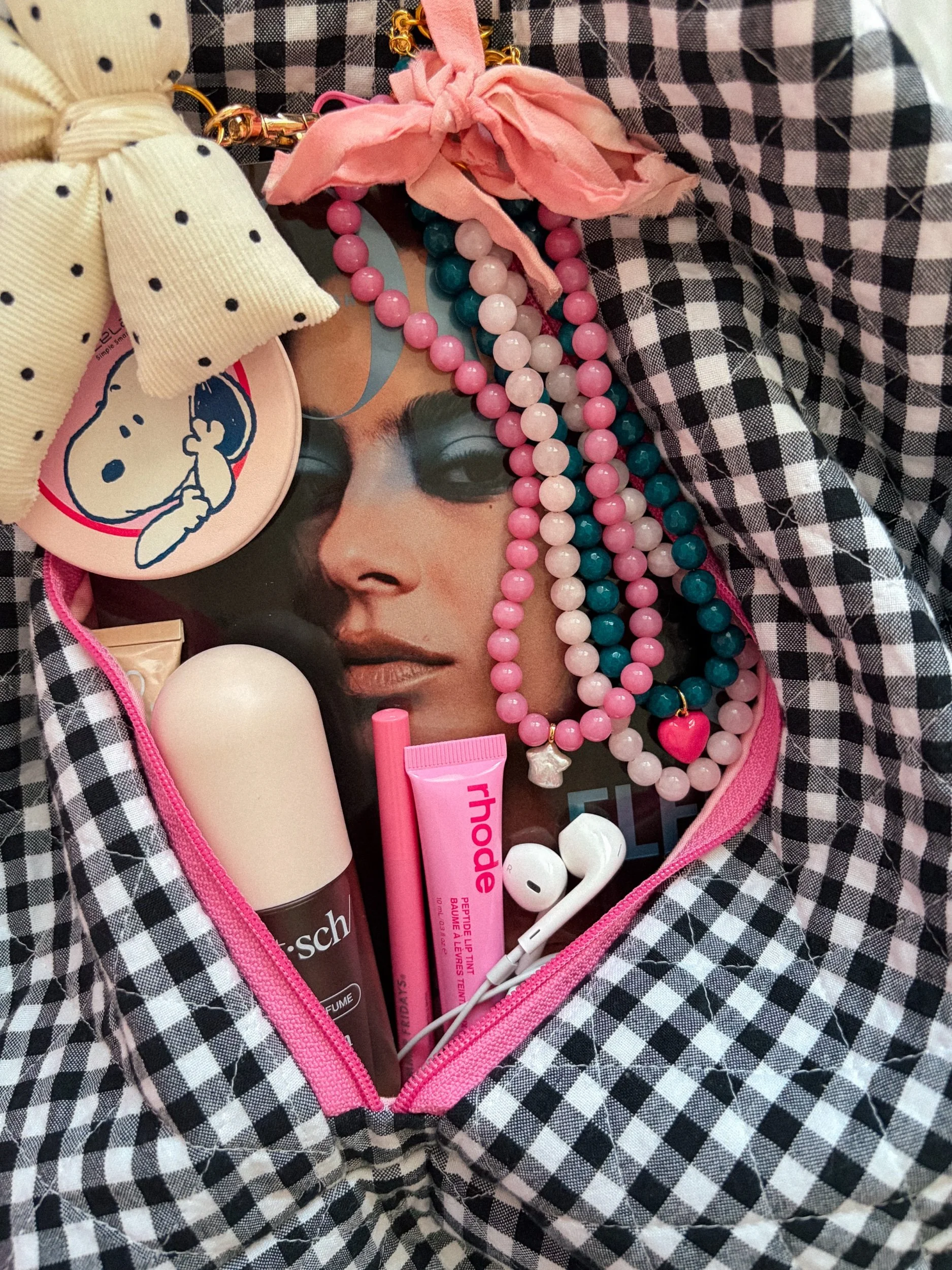 A backpack filled with various items including jewelry, makeup, and headphones. The backpack has a black and white checkered pattern with a pink zipper.