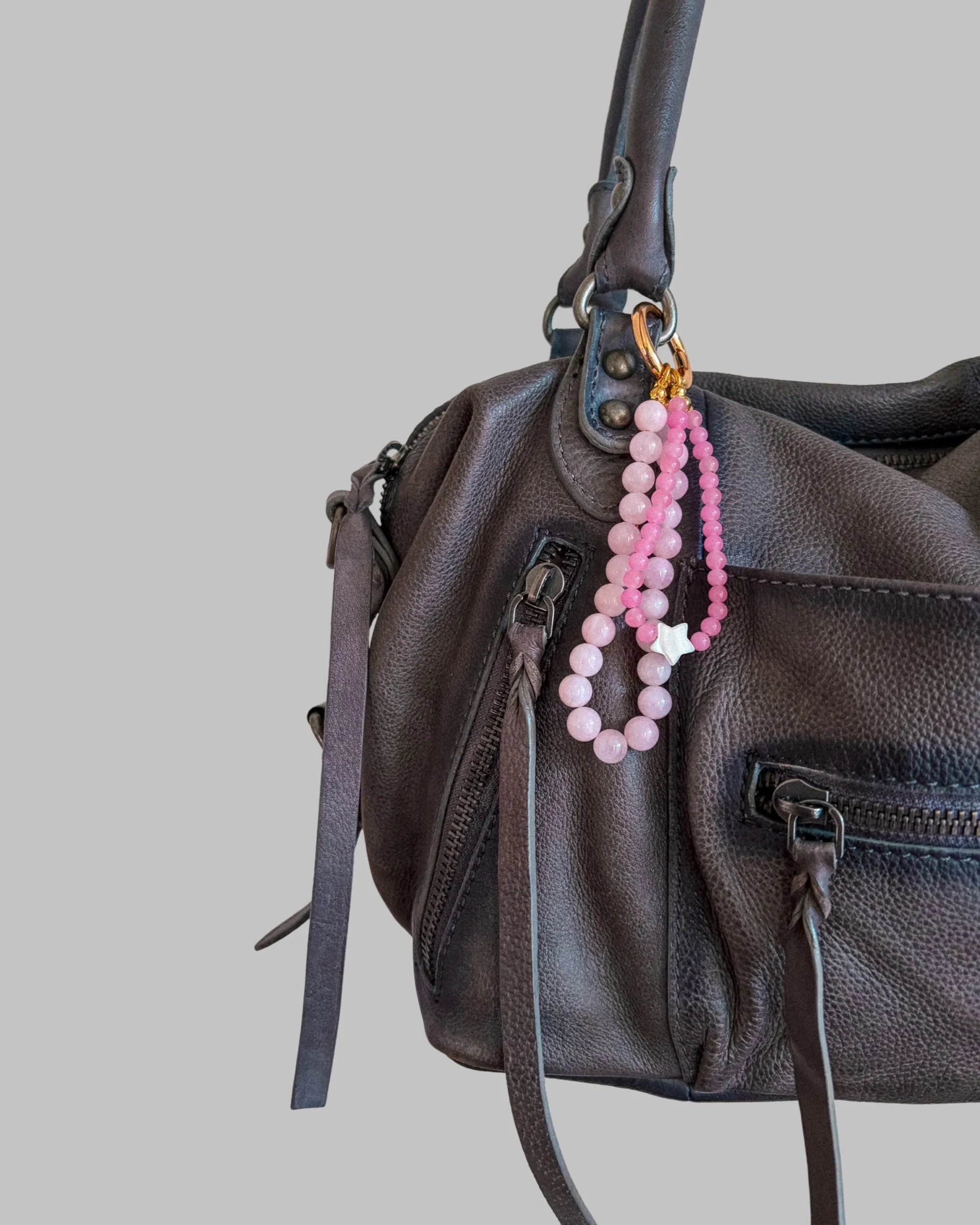 Wildflower Pink Beaded Bag Charm clipped to a gray leather handbag against a plain gray background