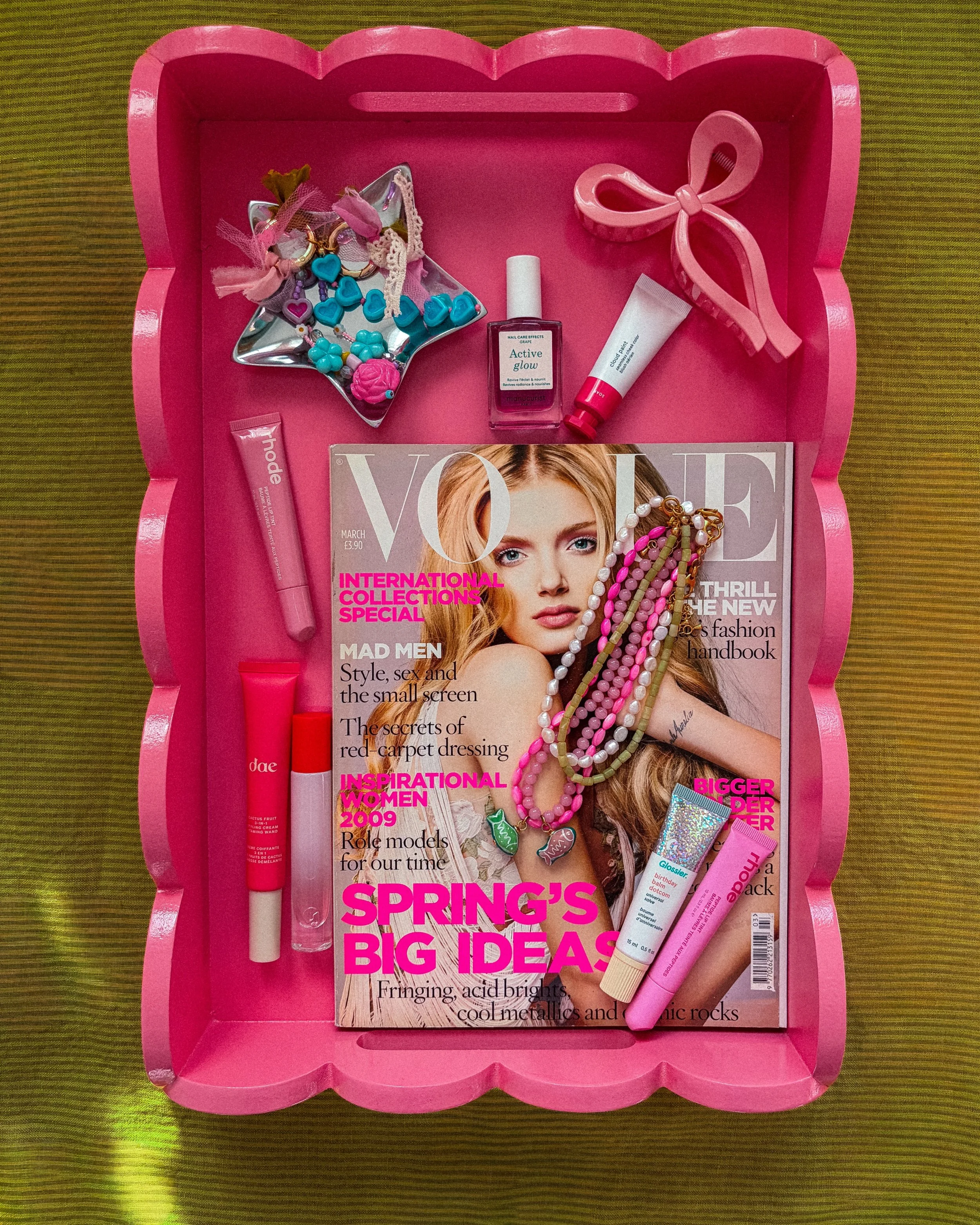 Pink tray with a magazine, pink lipstick, and various beauty products and accessories on top