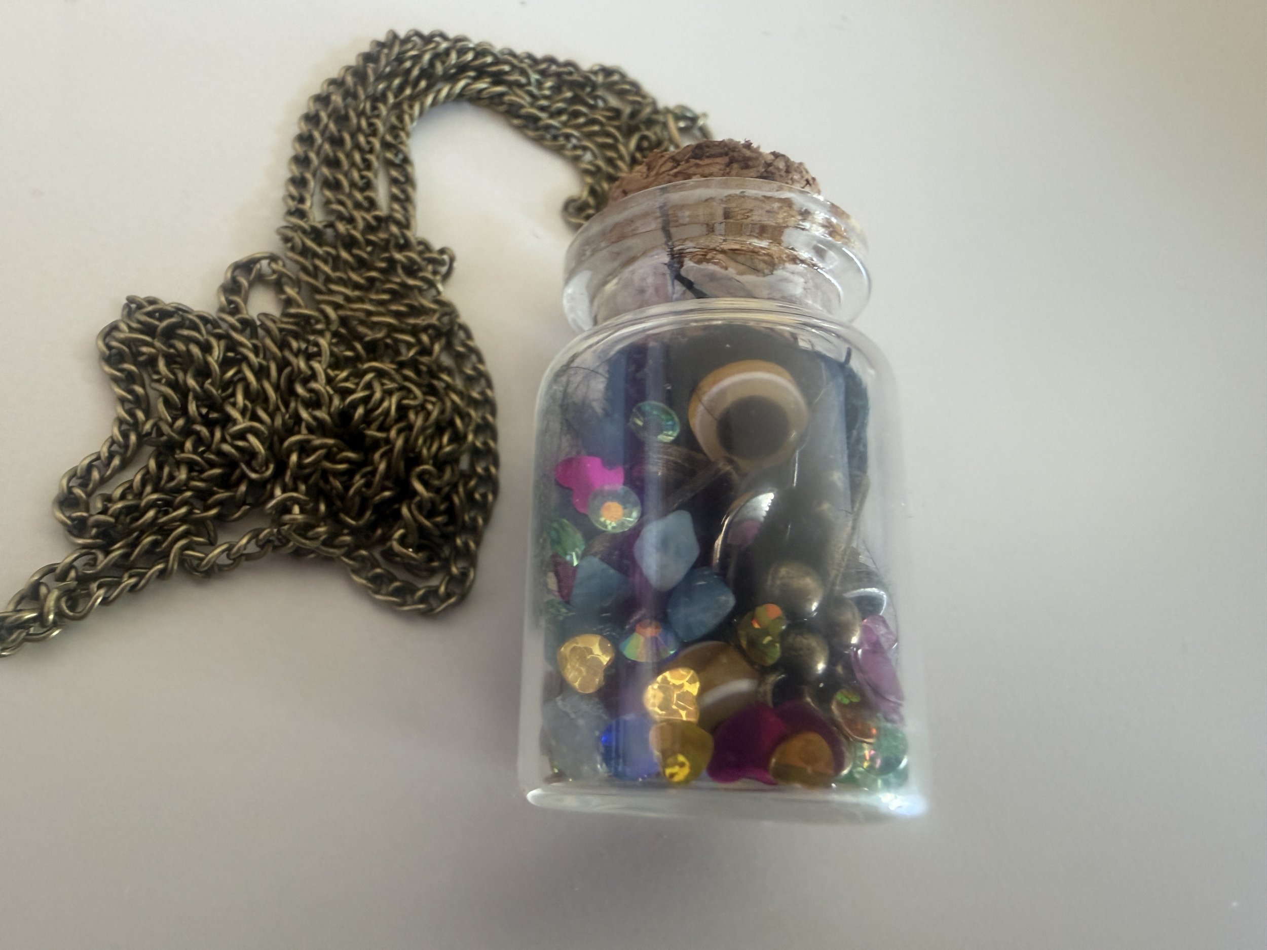A silver chain necklace next to a transparent container filled with colorful, reflective sequins.