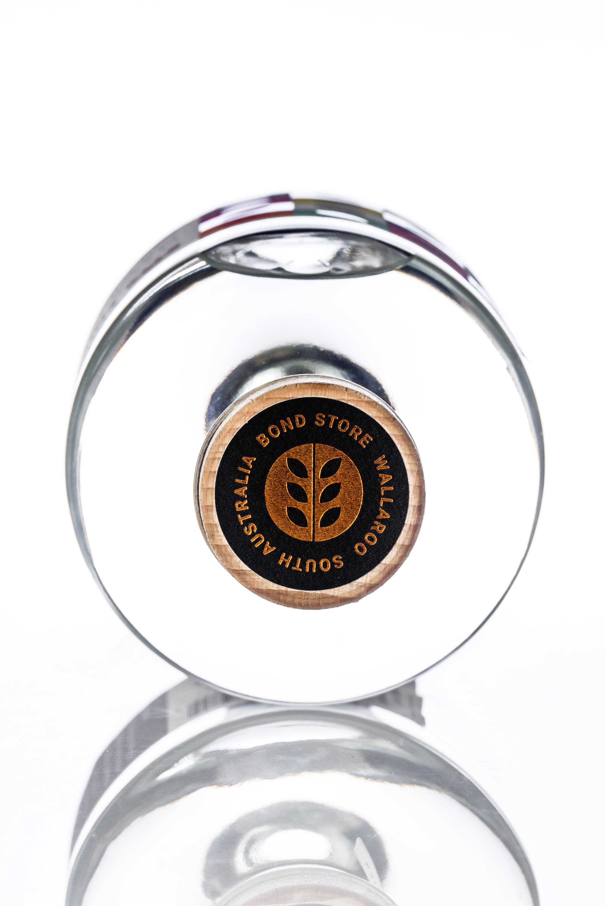 Top view of a wine bottle with a circular black and orange label, inside a clear glass wine holder.