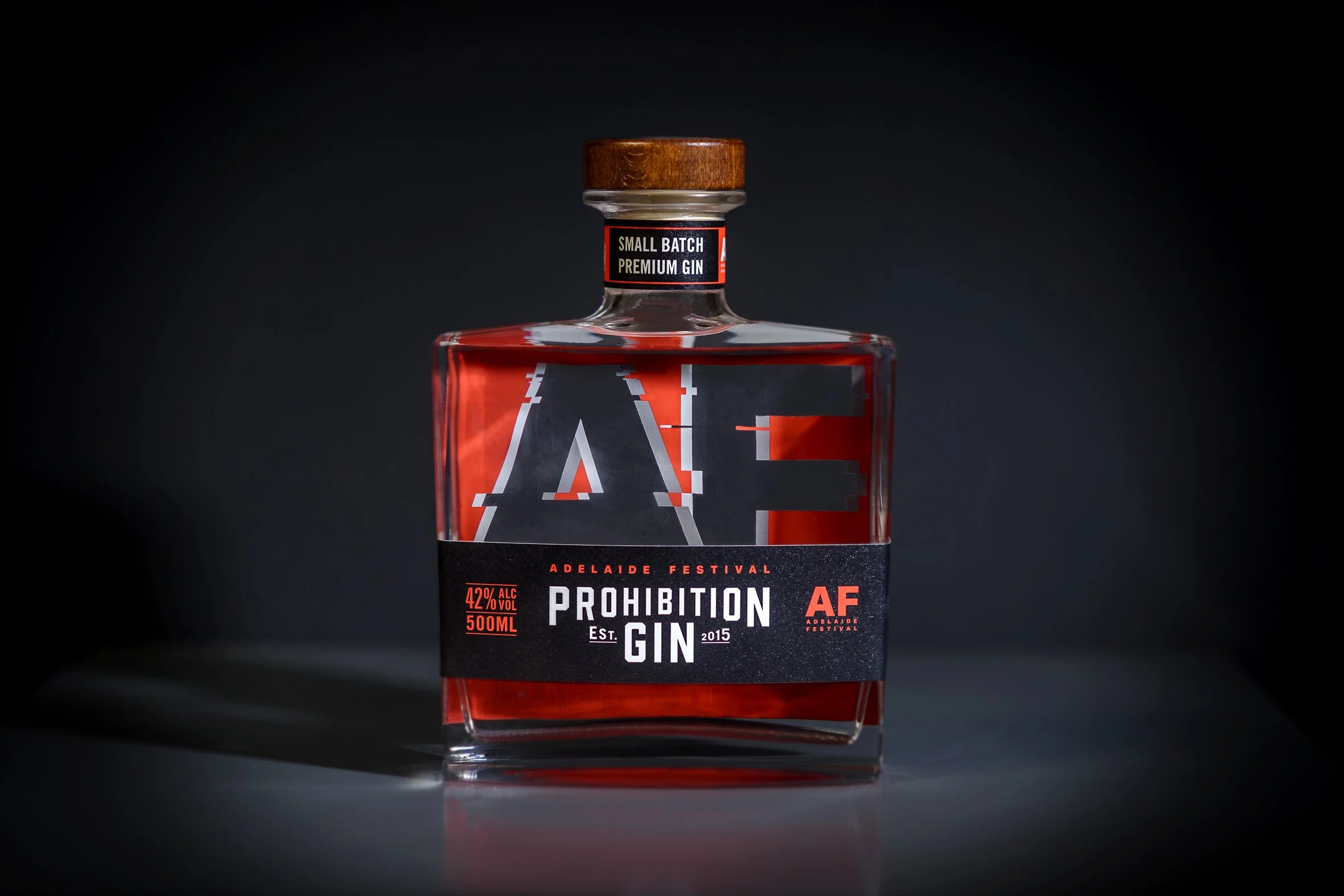 A bottle of prohibition gin with a black and red label, wooden cap, and bold text, set against a dark background.