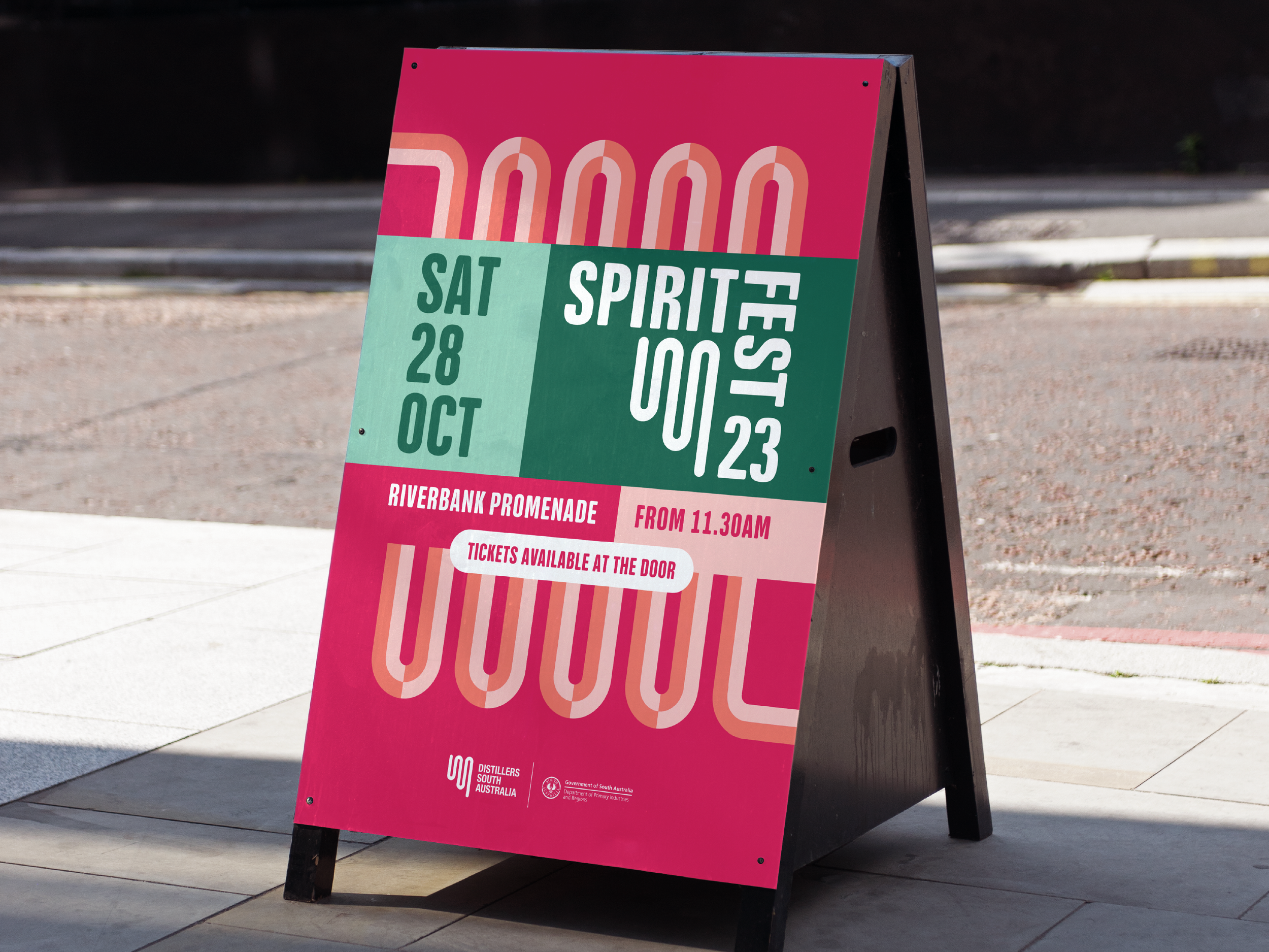 Pink and green sidewalk sign promoting an event called '1000 Fest' on October 28th at Riverbank Promenade in South Australia, with additional event details and logos at the bottom.