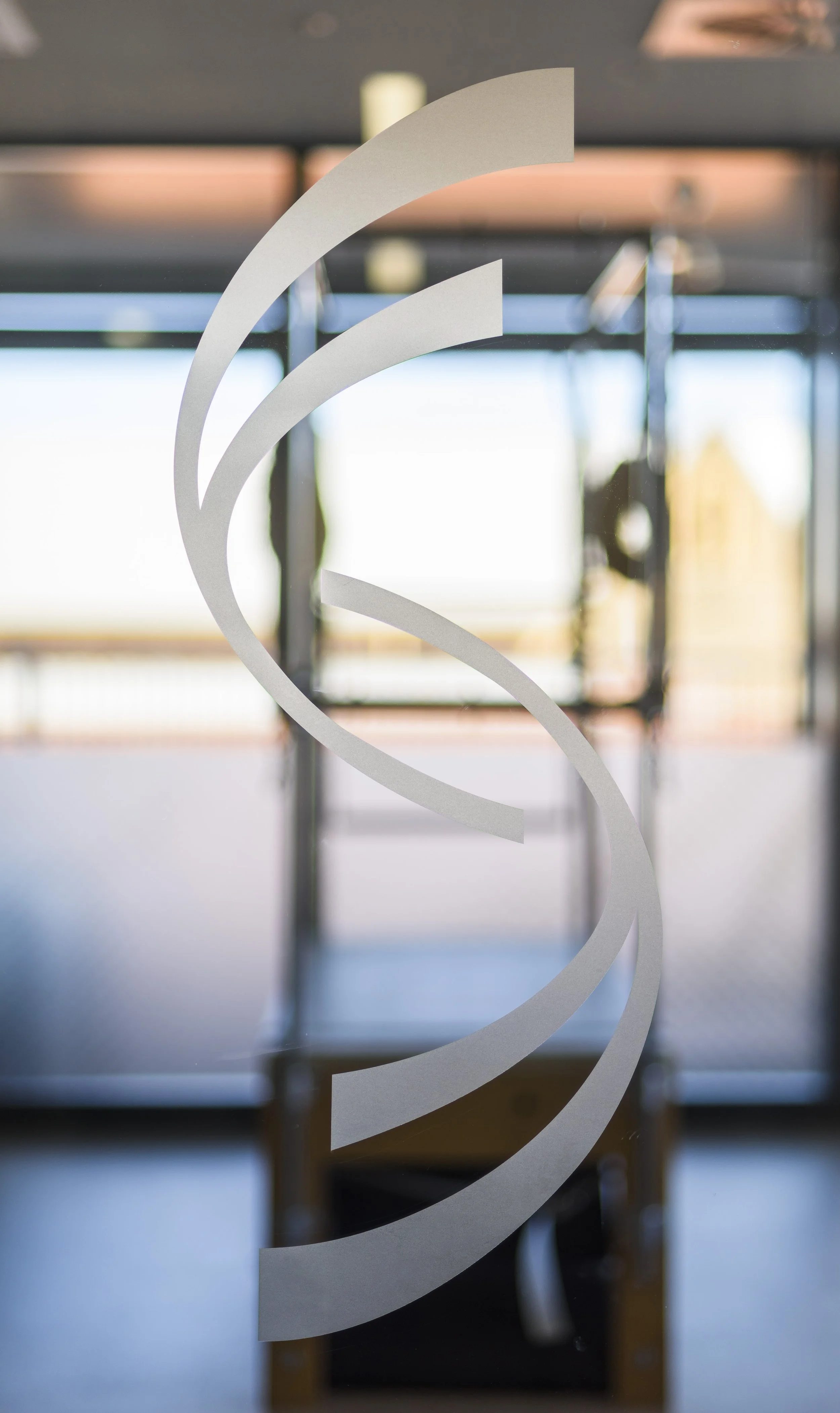 Close-up of a glass door with frosted design, showing a blurred indoor space and windows with natural light in the background.