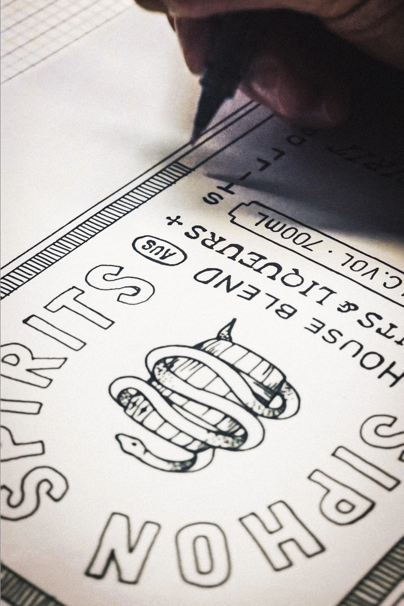 Close-up of a textured paper with printed and drawn elements, including a cartoonish snake illustration and text, with part of an object or hand holding the paper visible at the top.
