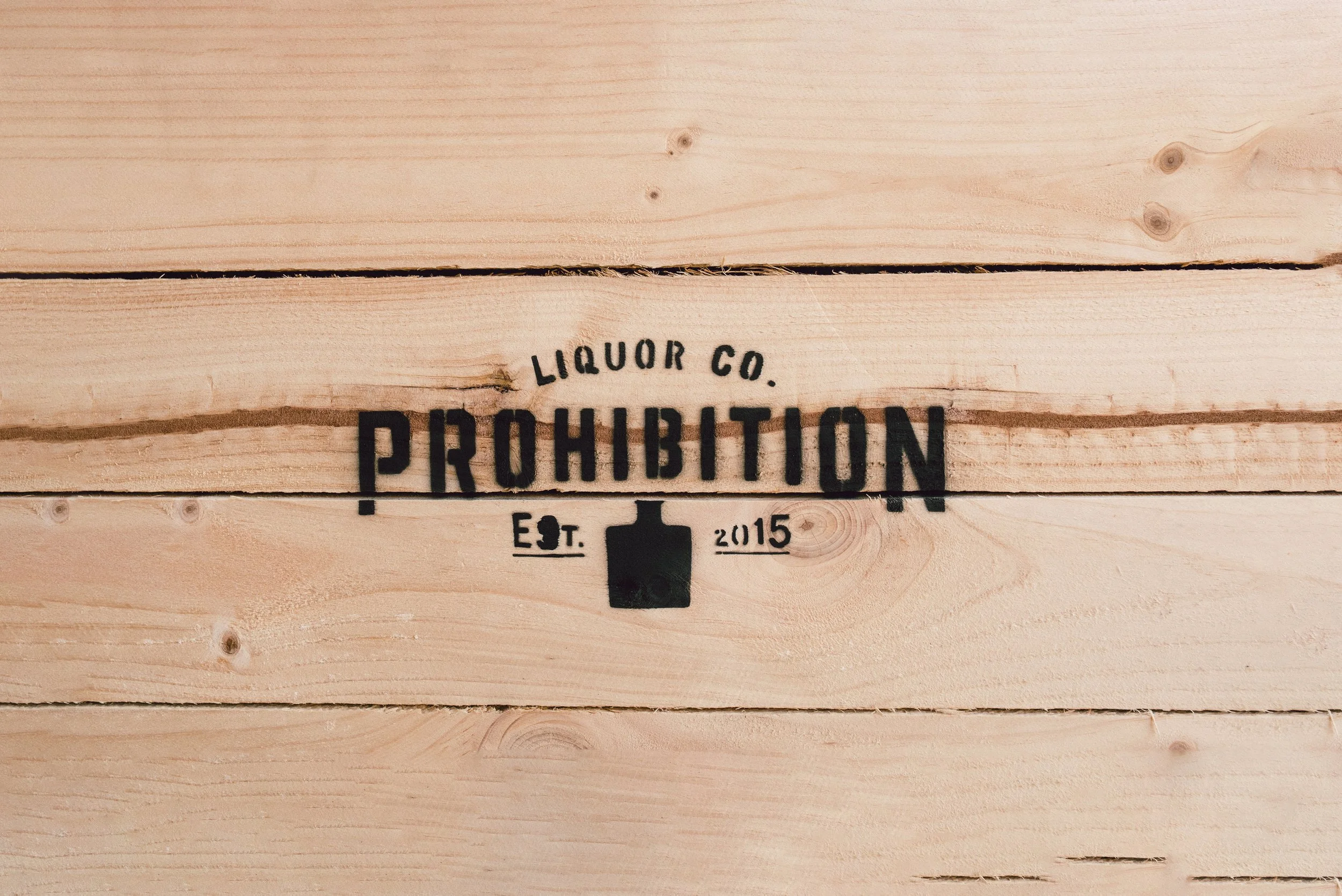 A wooden surface with a printed logo that reads 'Liquor Co. Prohibition Est. 2015' and features a silhouette of a whiskey bottle.