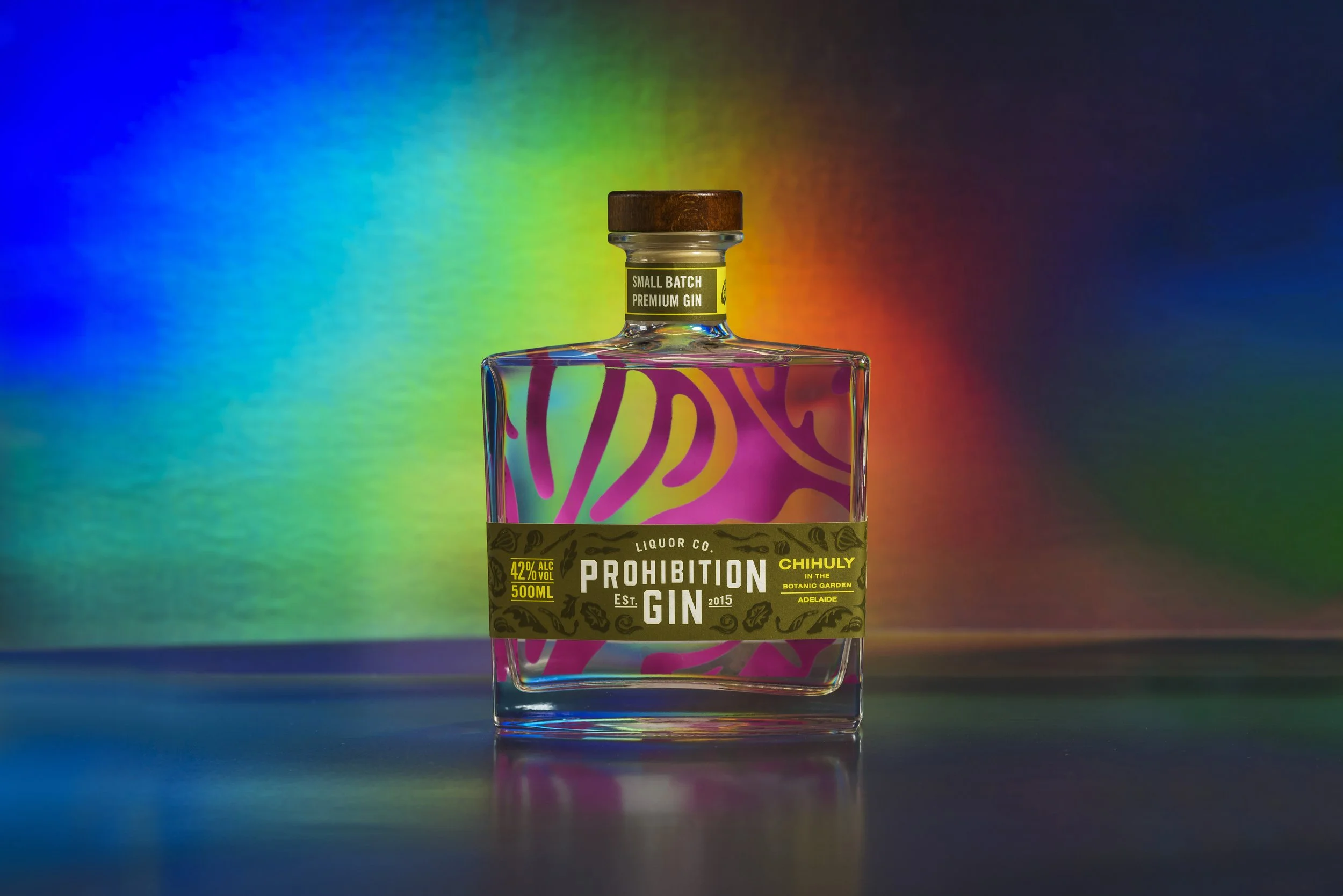 A bottle of gin with colorful swirling design on the label, set against a vibrant rainbow-colored background.