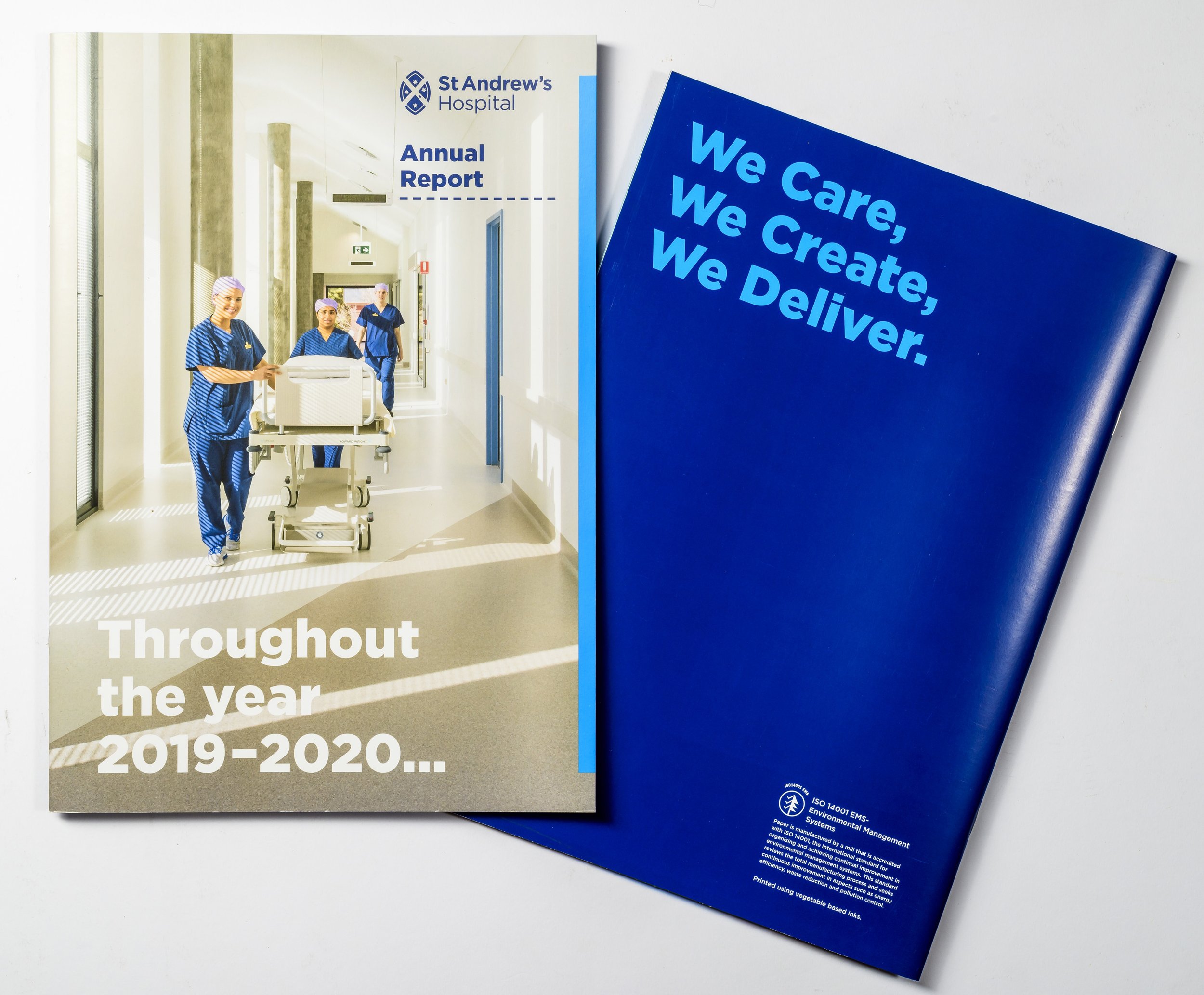 A hospital annual report booklet from St Andrews Hospital, with a cover photo of medical staff pushing a patient on a gurney in a hospital corridor, and a blue sign with the message, "We Care, We Create, We Deliver".