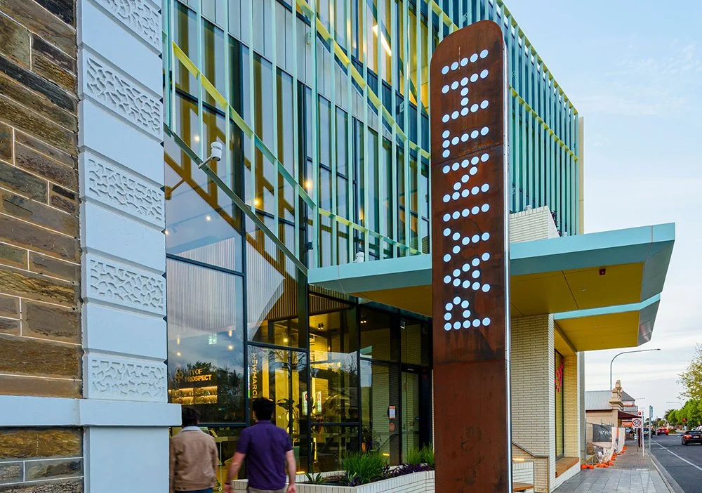 Modern building with the word 'BANK' in dotted lights on a tall rusty sign