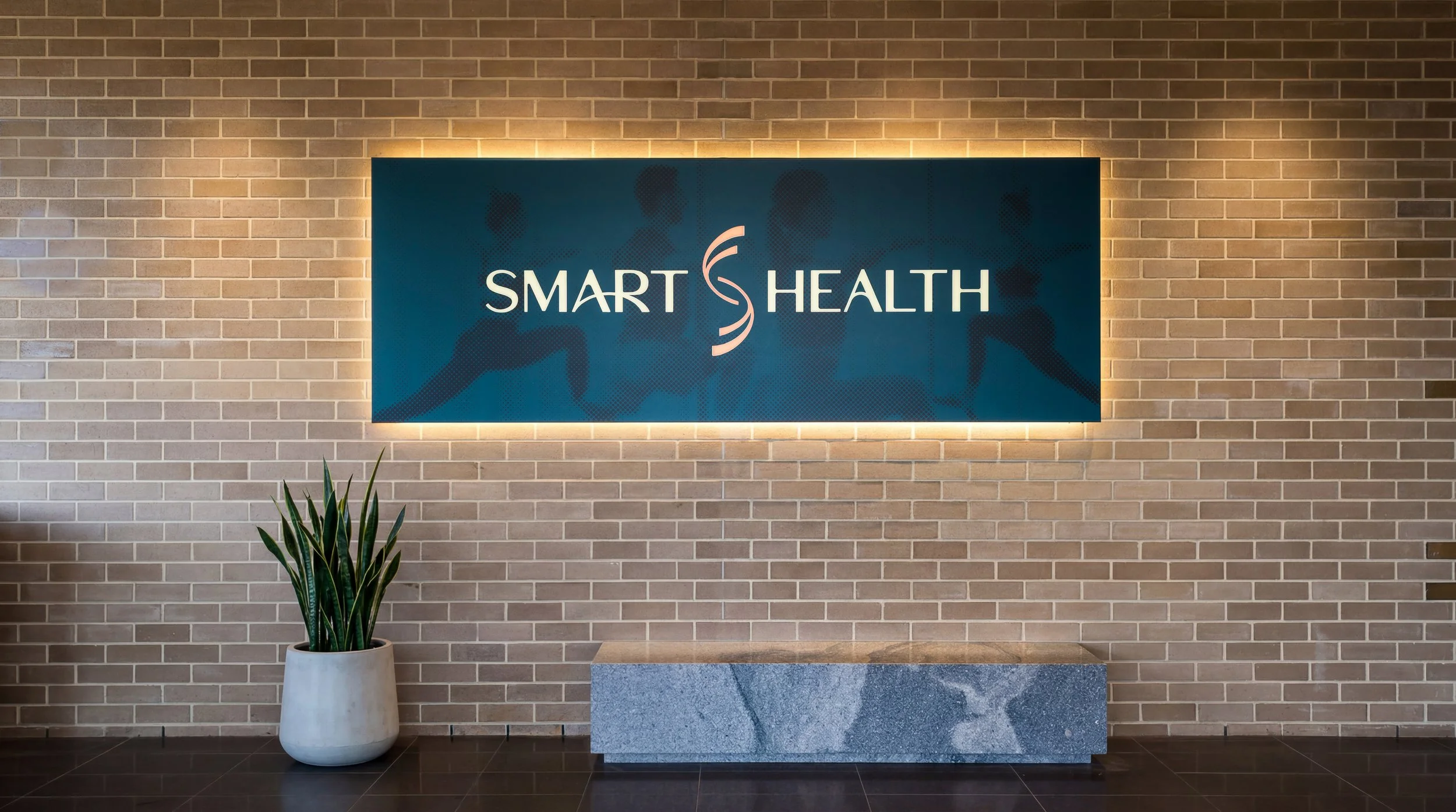 Interior of a healthcare facility with a brick wall, a sign that says 'Smart Health' with a DNA strand graphic, a potted plant, and a stone pedestal.