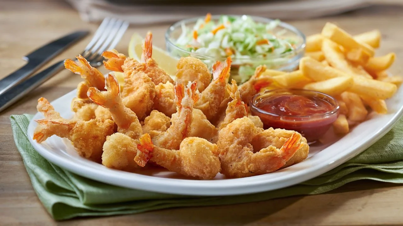 Fried shrimp with cocktail sauce, French fries, and coleslaw on a white plate