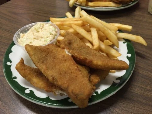 Plate of fried fish fillets, French fries, and coleslaw, with a small container of coleslaw on the side.