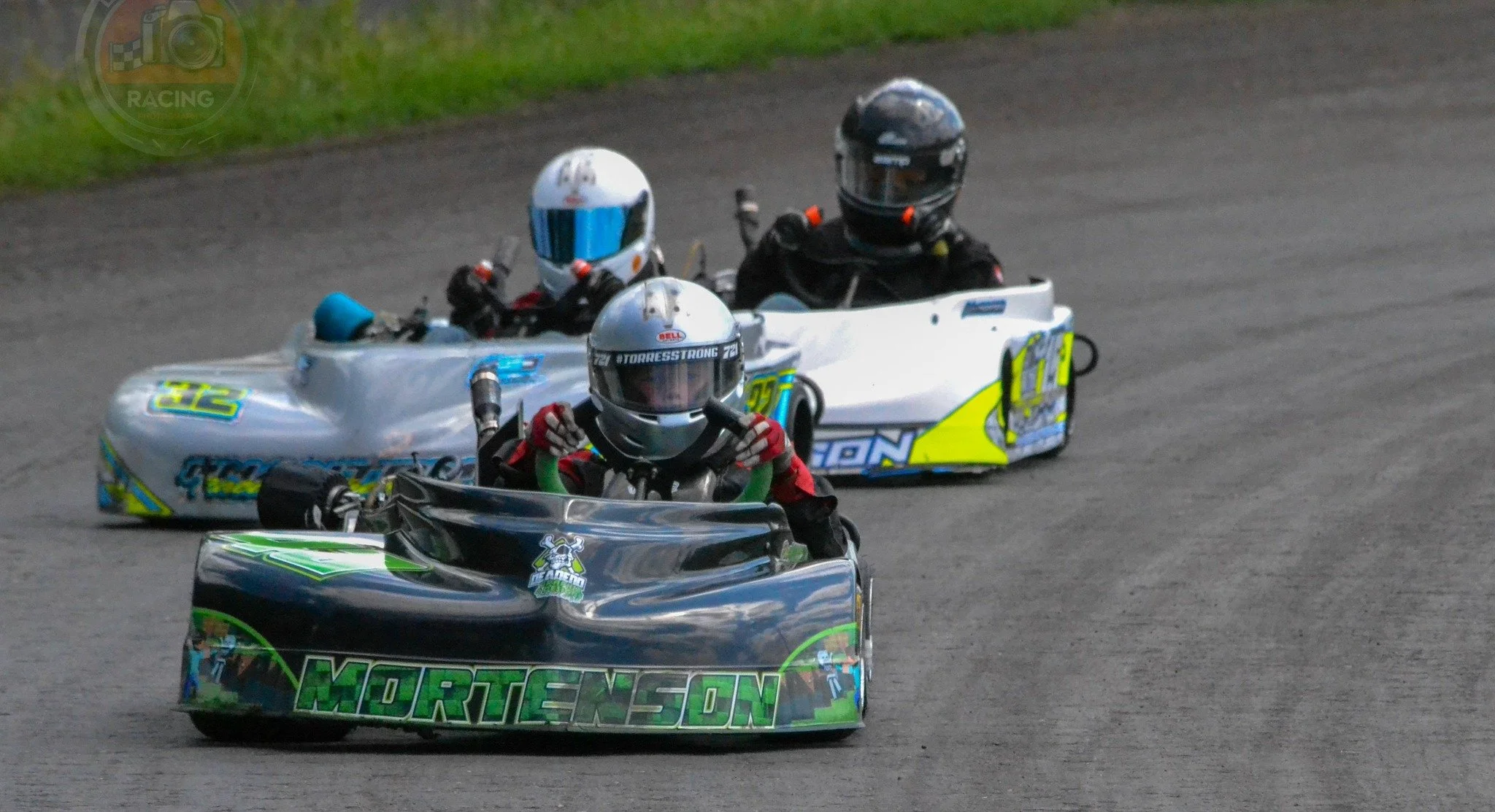 Three go-karts racing on a track, with drivers wearing helmets and racing suits.