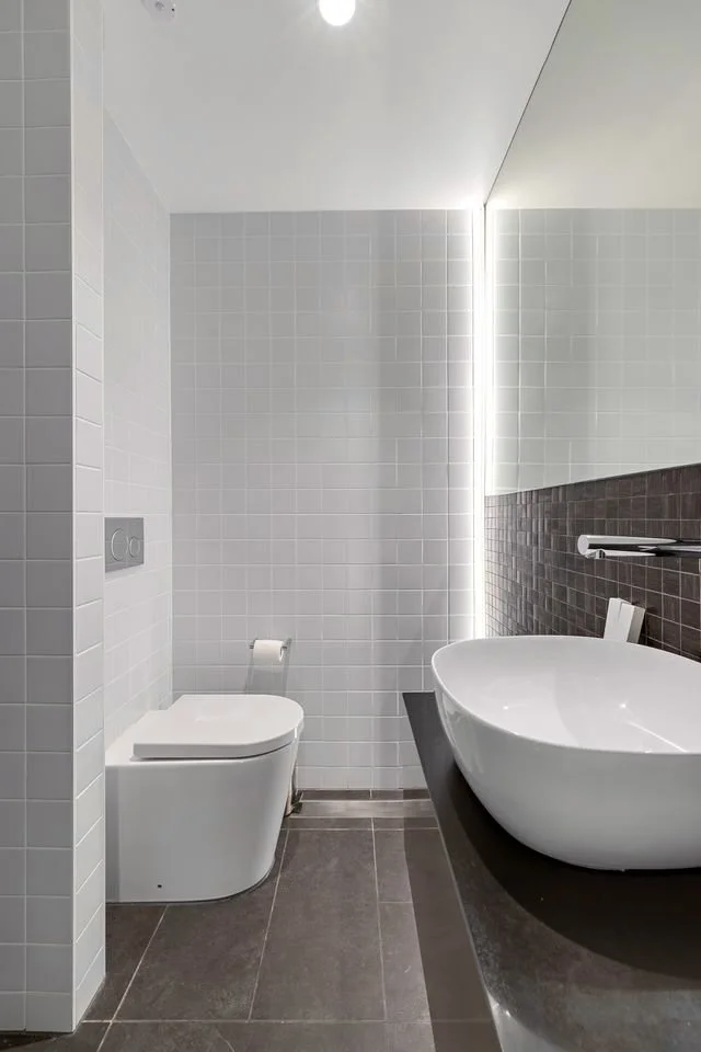 Modern bathroom with a wall-mounted toilet, a vessel sink on a black countertop, and a large mirror with integrated lighting.