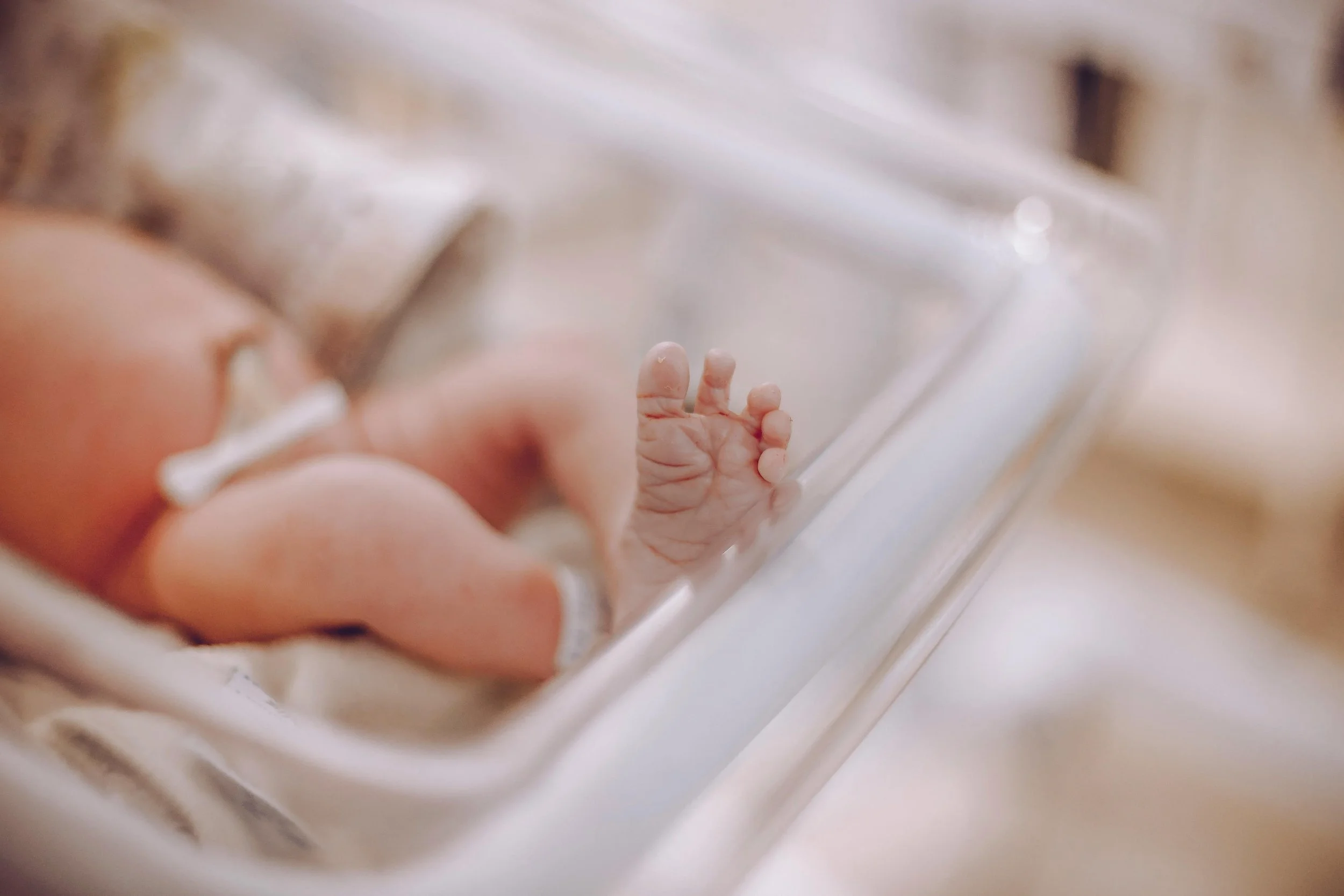 Close-up of a newborn baby's tiny hand gripping a person's finger, with soft focus and warm lighting.
