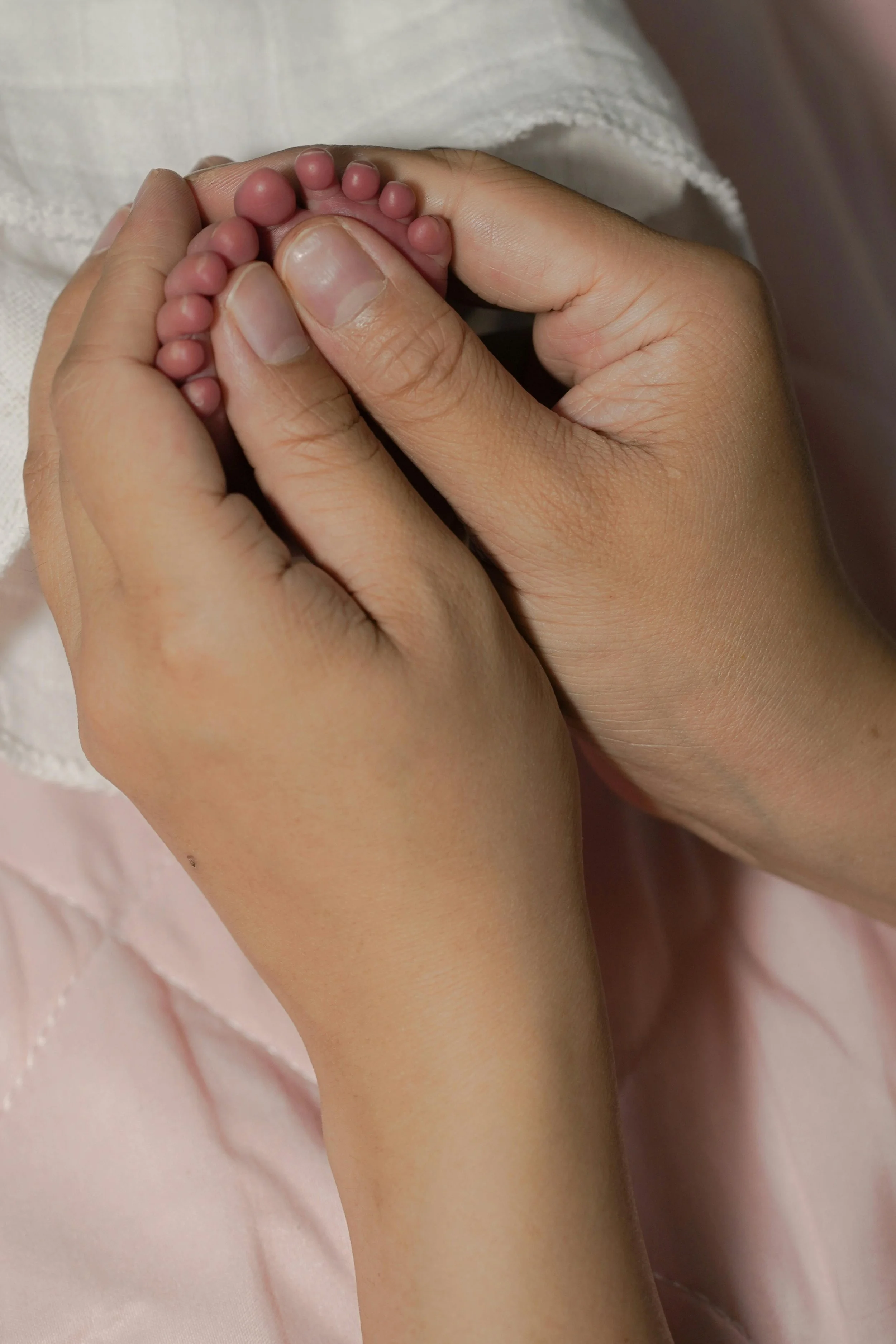 A person gently holding a baby's tiny toes with their fingers against a soft pink background.