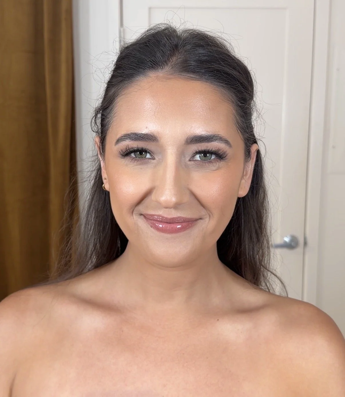A young woman with long, dark hair and light skin, smiling at the camera, with minimal clothing visible.