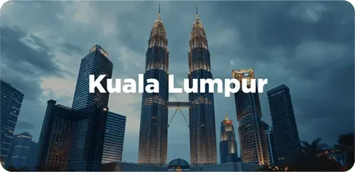 Nighttime view of Kuala Lumpur with the Petronas Towers and surrounding skyscrapers under a cloudy sky.