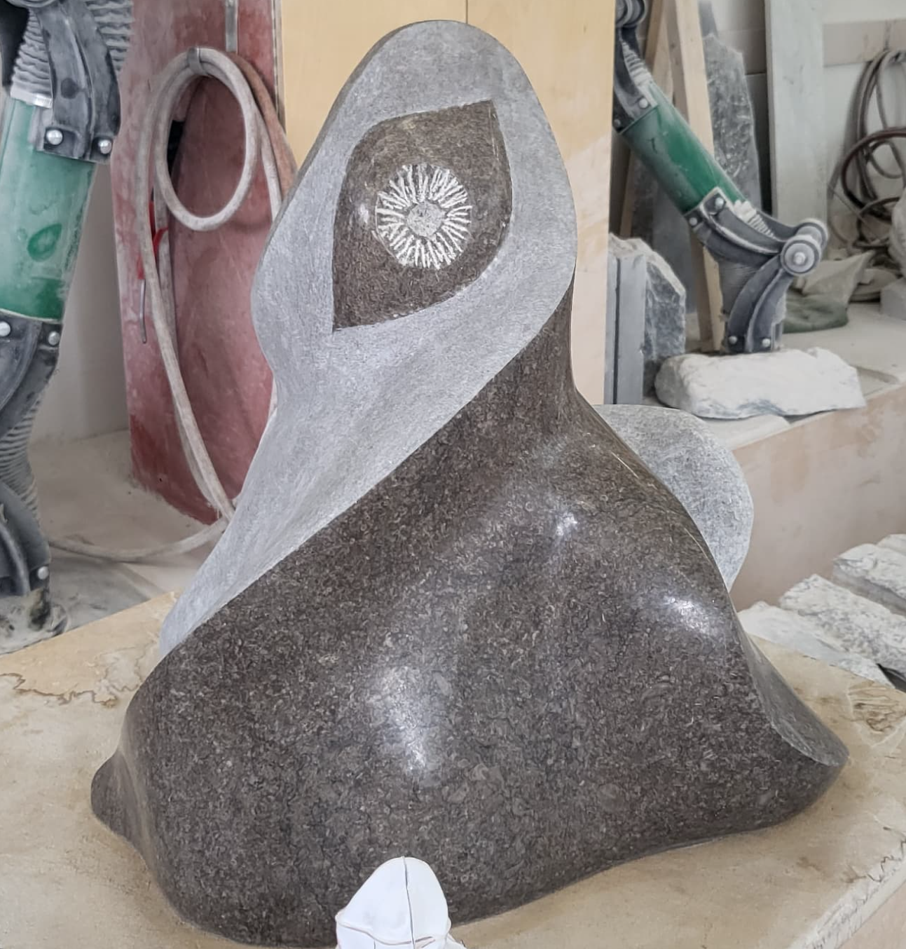 Sculpture abstraite en pierre avec une forme courbée et une tête stylisée, dans un atelier de sculpture.