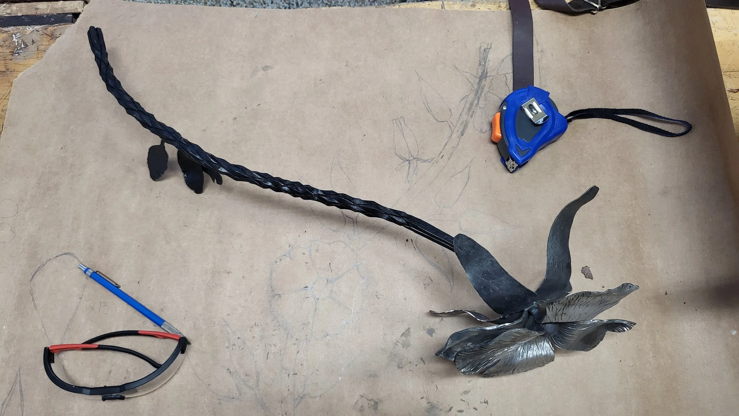 Une sculpture métallique d'une fleur, posée sur une surface en bois avec divers outils et objets autour.