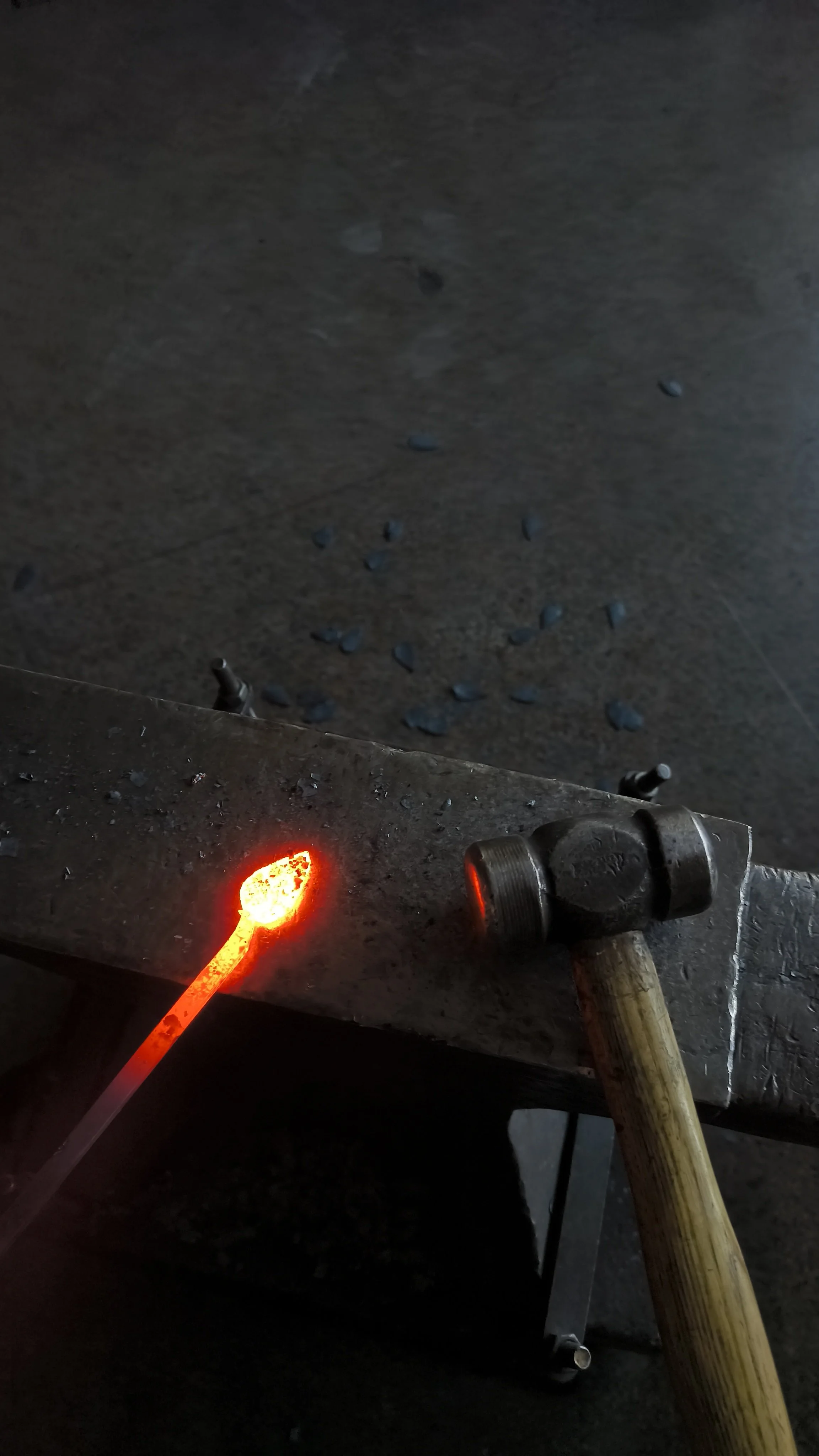 Un marteau repose sur une table de travail en métal, à côté d'une pince, avec un métal rougeoyant chaud devant, et des débris métalliques sur le sol.
