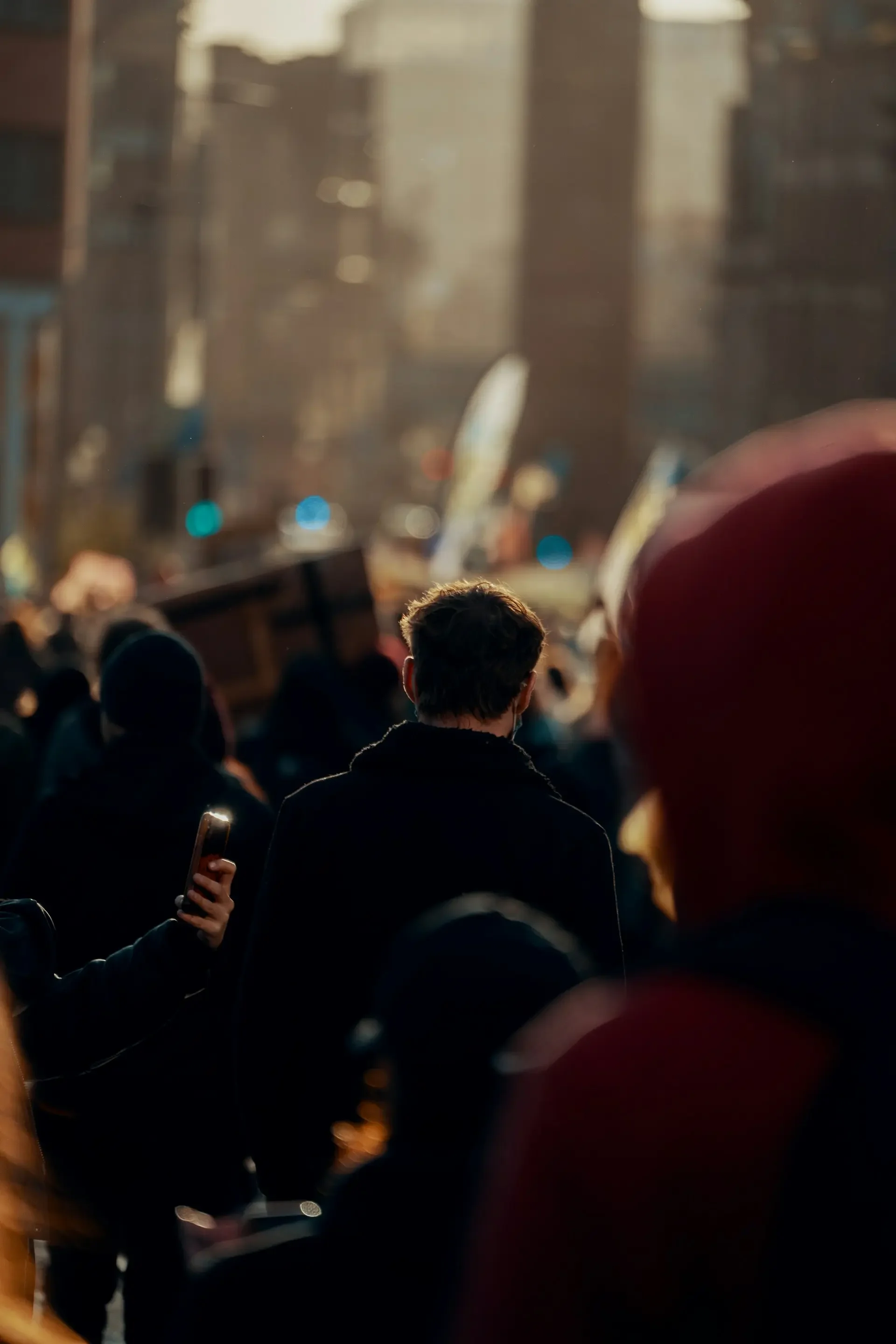 People gathered in a city street during sunset, with blurred skyscrapers and city lights in the background.