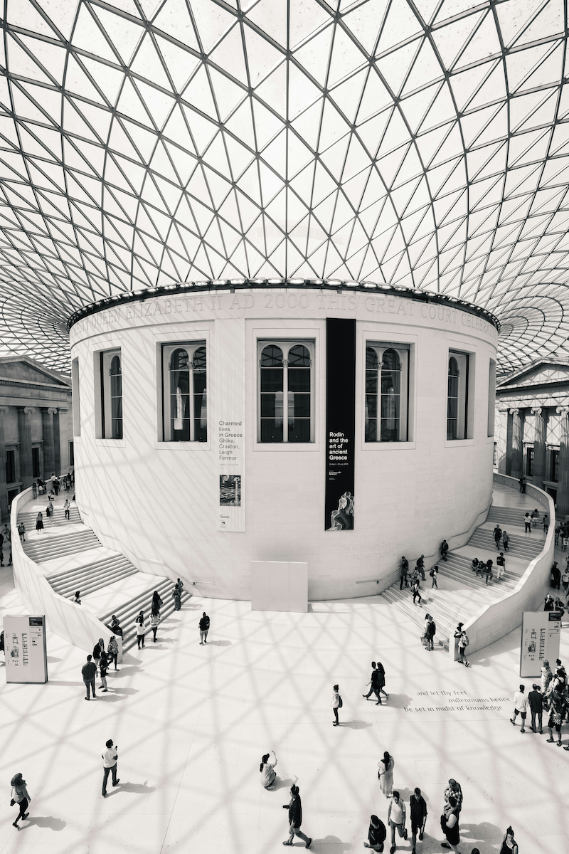 Interior of a modern museum with a large circular structure and a glass geometric roof, with people walking around.