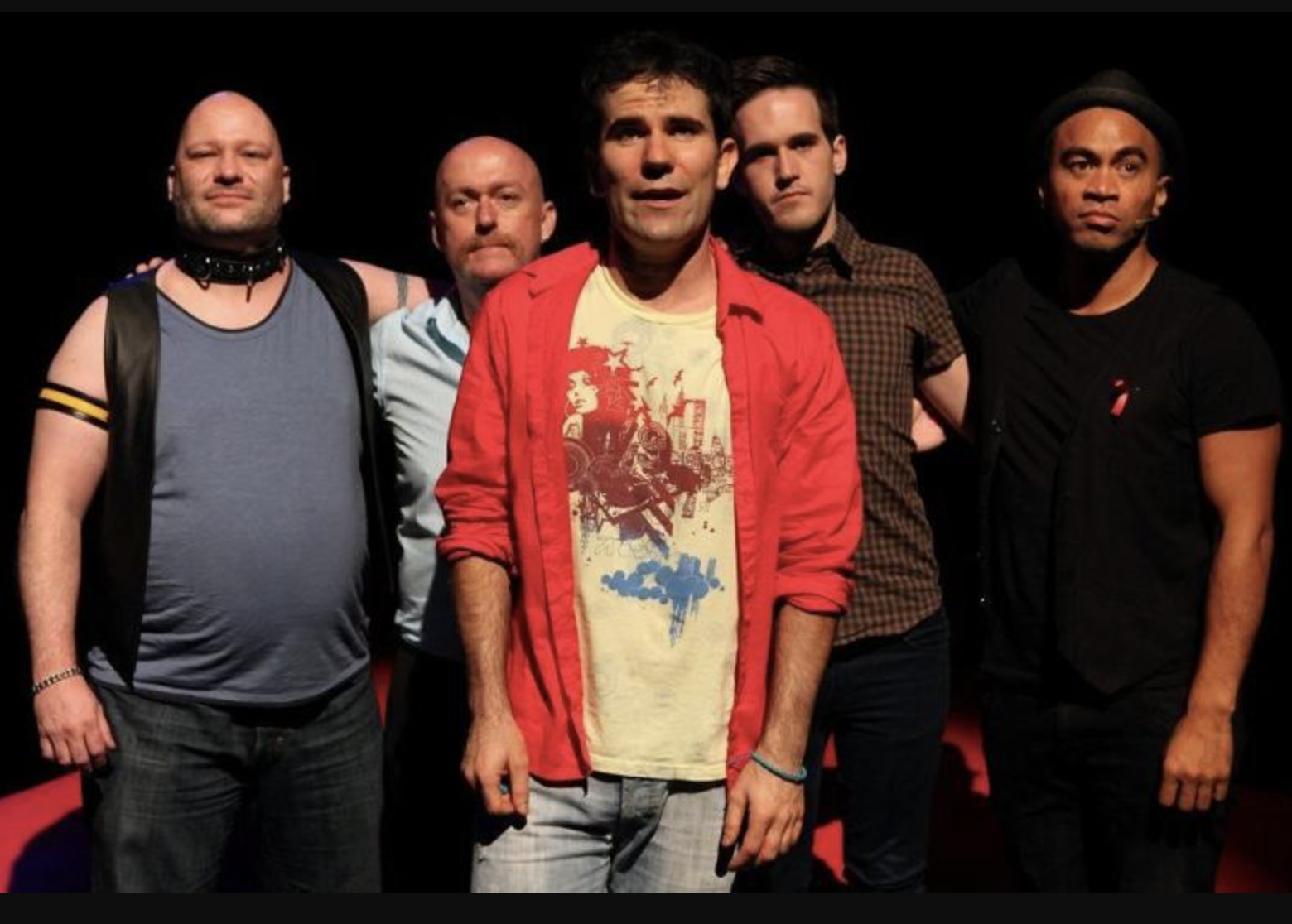 Five men standing together against a black background, dressed casually, with serious expressions.