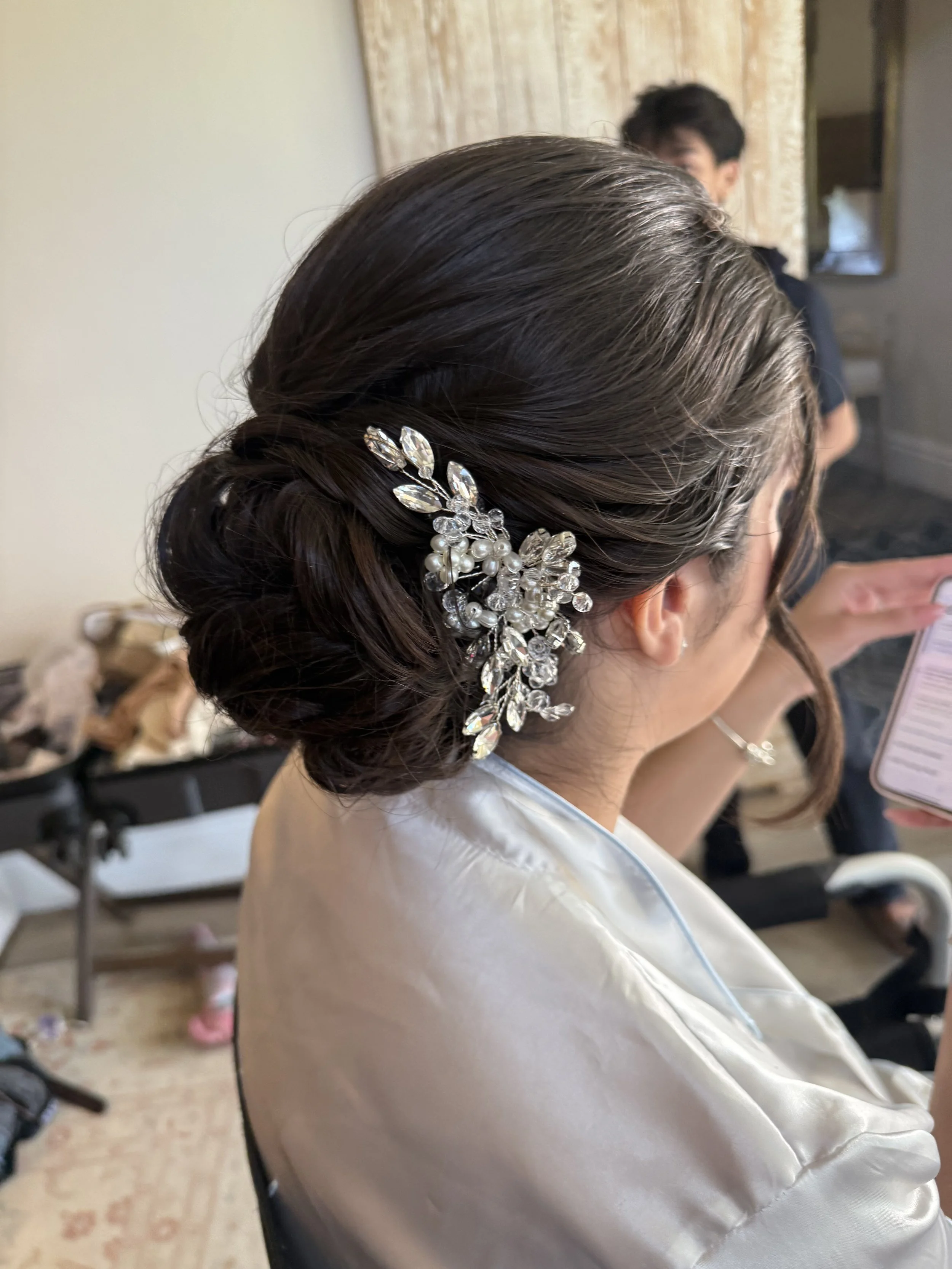 Elegant low bridal bun with a crystal hair accessory, styled for a classic wedding look. 