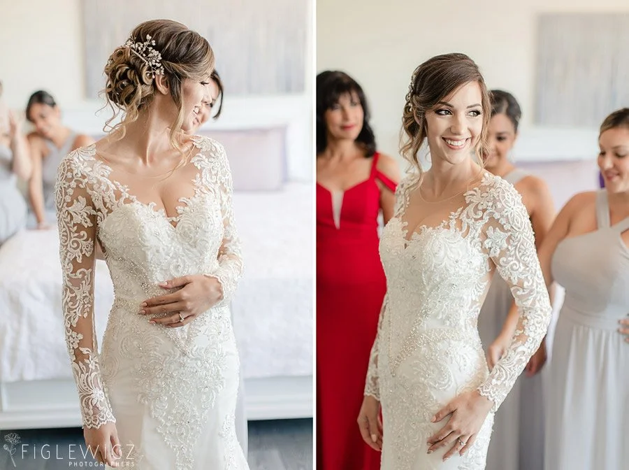 Bride in a long-sleeve lace wedding gown with a soft glam bridal up and hair accessory smiling and looking to the side while getting ready with breidesmaids in the background.