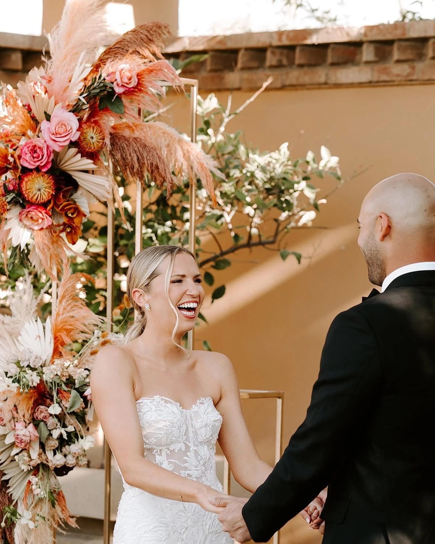 A laughing blonde bride with a low ponytail and soft glam makeup looking at her groom during a wedding in Palm Springs.