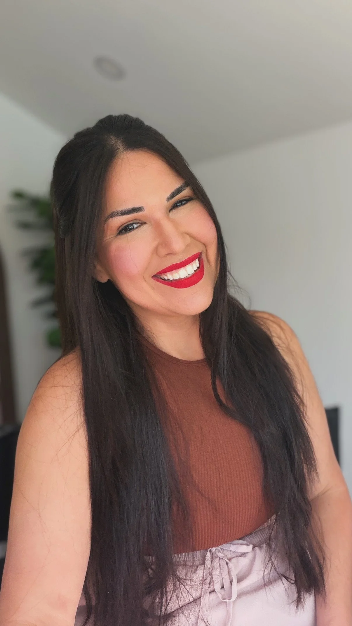 Head short of Jazmin Uranga with long dark hair wearing soft makeup and a bold red lip smiling at the camera.