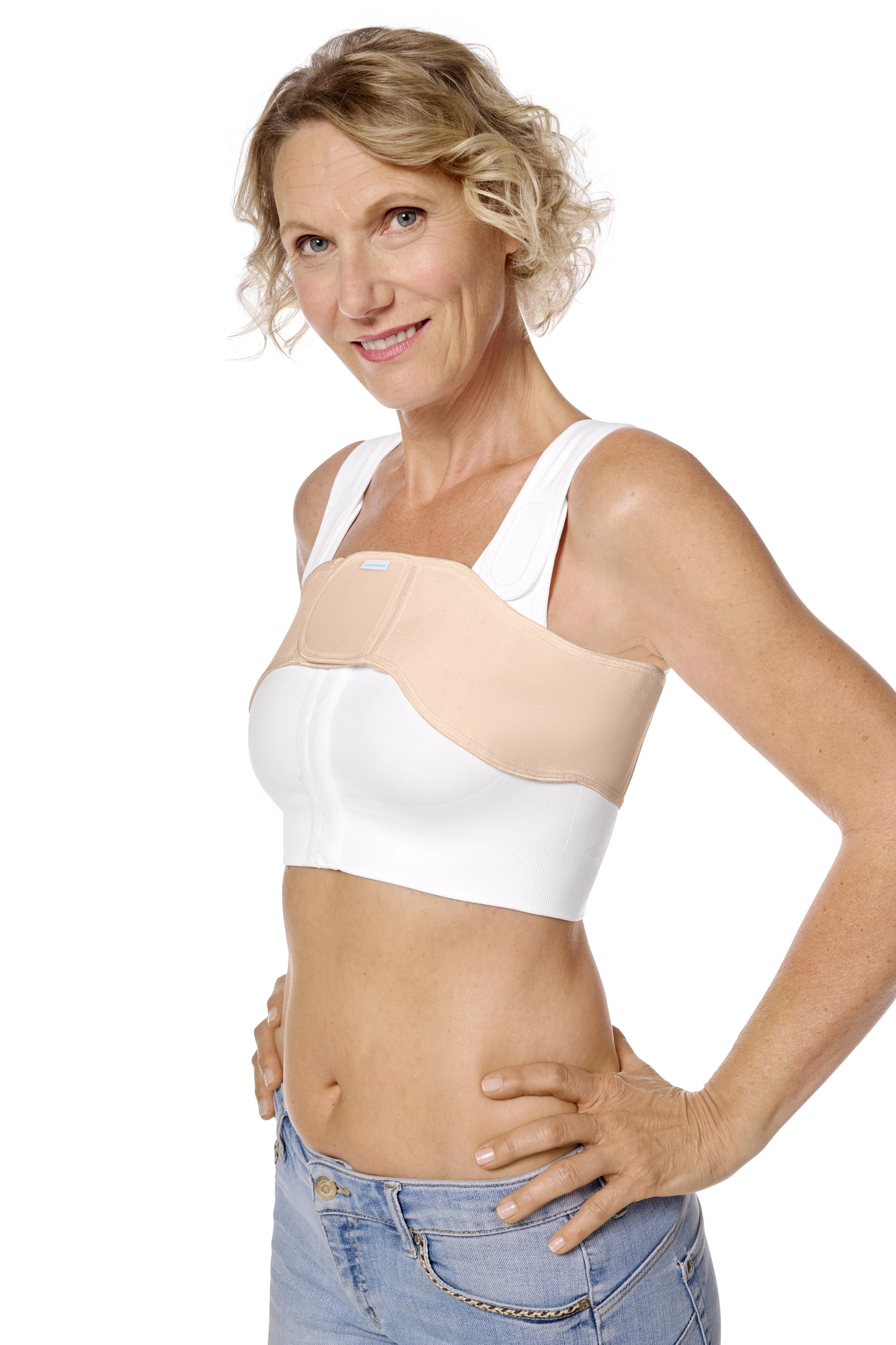 A woman with short curly blonde hair wearing a white top and blue jeans, smiling, with a beige medical posture brace around her chest.