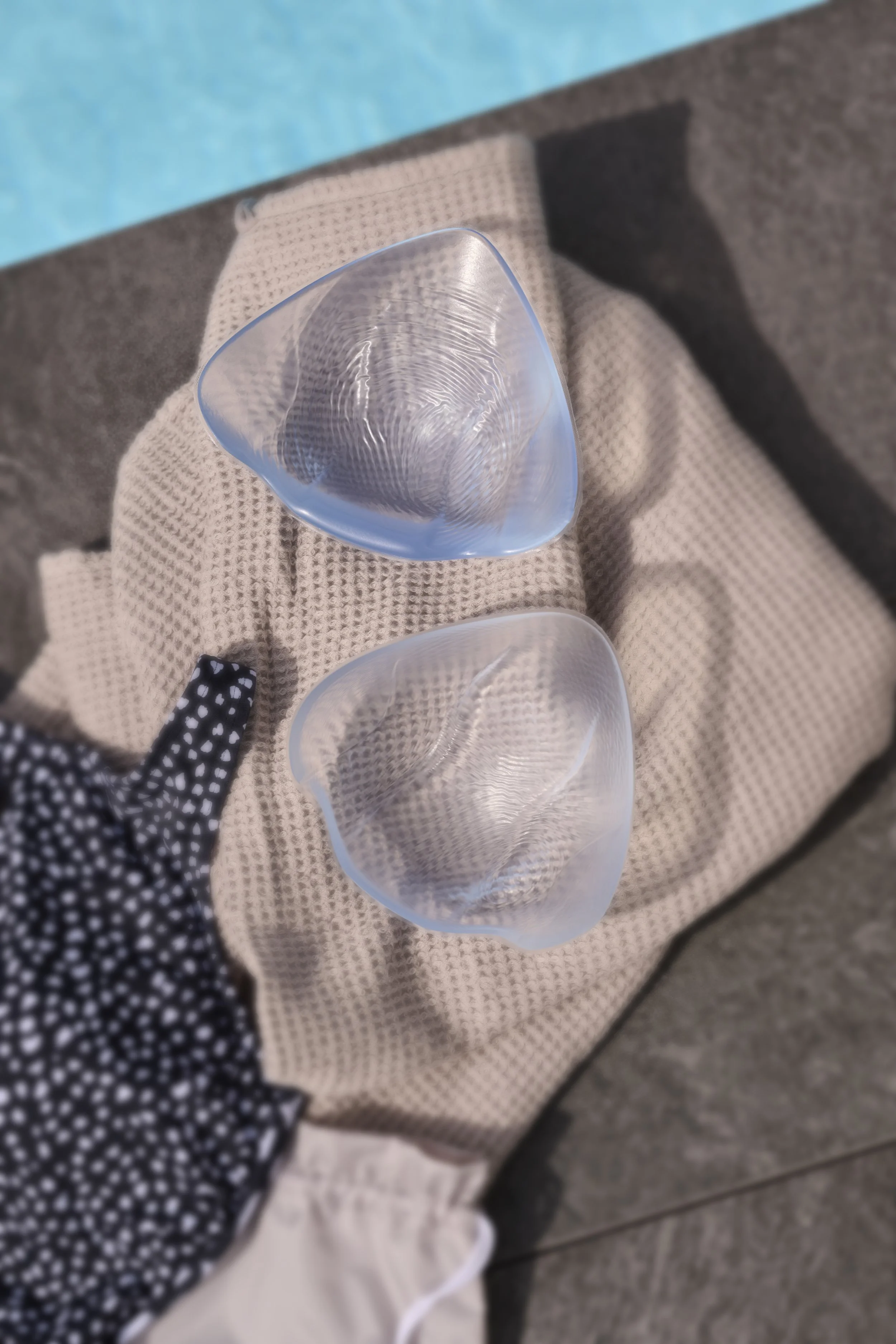 A close-up view of a hand wearing a black and white polka dot glove holding a glass of water, with two other empty glasses on a beige textured cloth, a person's lap, and a grey floor in the background.