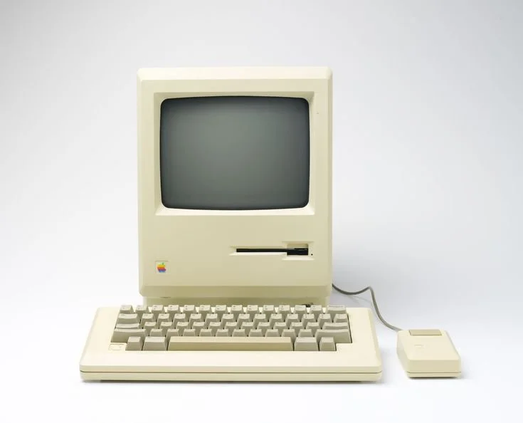 A vintage Apple Macintosh computer with a CRT monitor, keyboard, and mouse, all in beige color.
