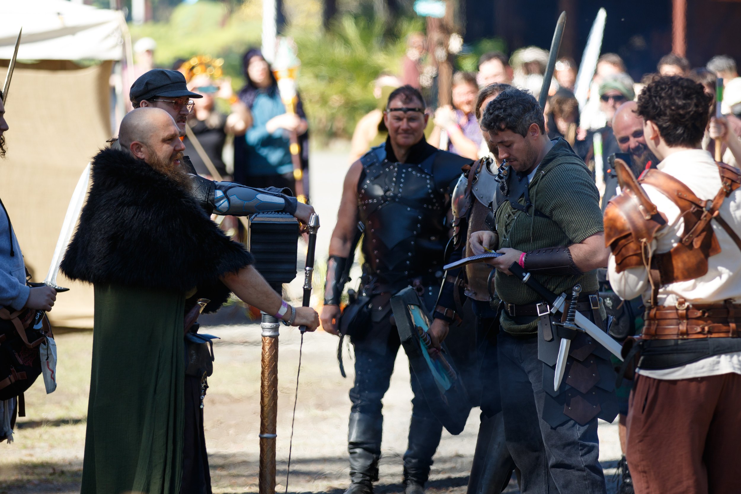Group of people in medieval costumes engaging in a role-playing event outdoors, with some holding swords and wearing armor.