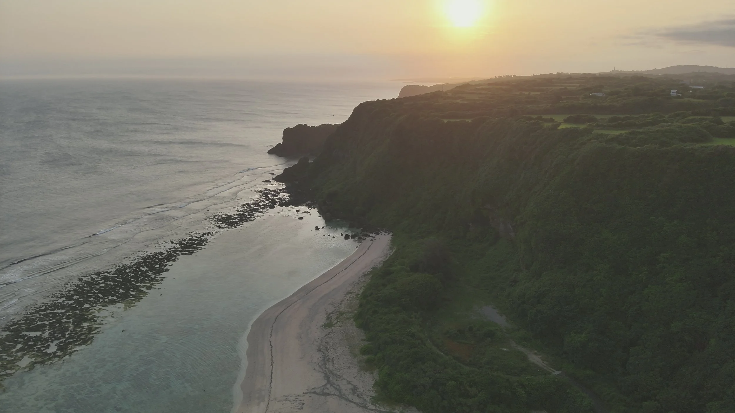 夕日が沈む海沿いの崖とビーチの風景。