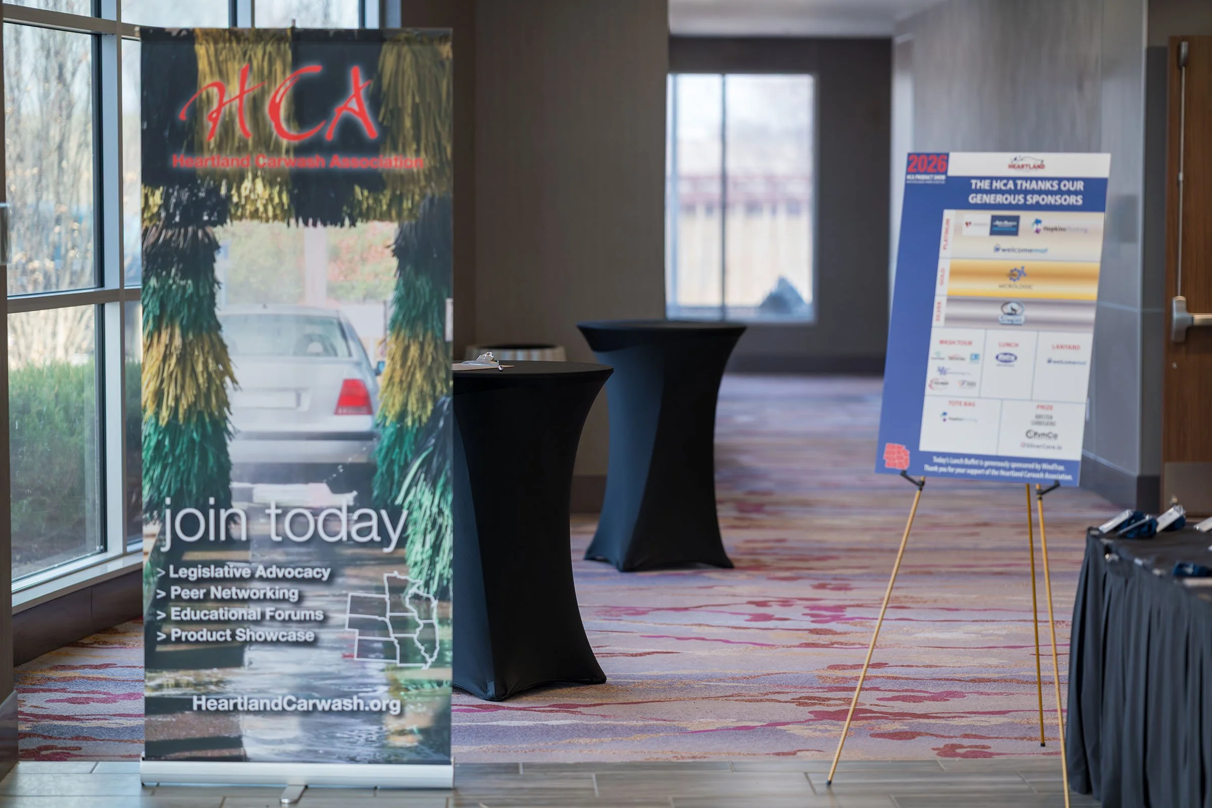 Event registration area with a Heartland Carwash Association banner and a standing sign listing sponsors, flags, and promotional materials.