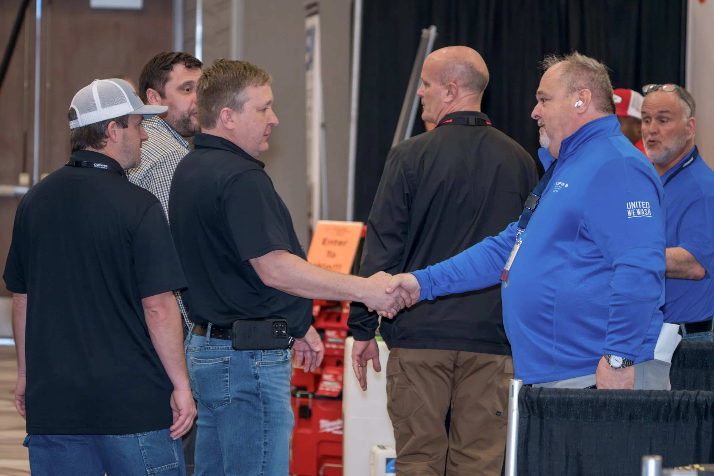 A group of men shaking hands and engaging in conversation at an indoor event or conference.