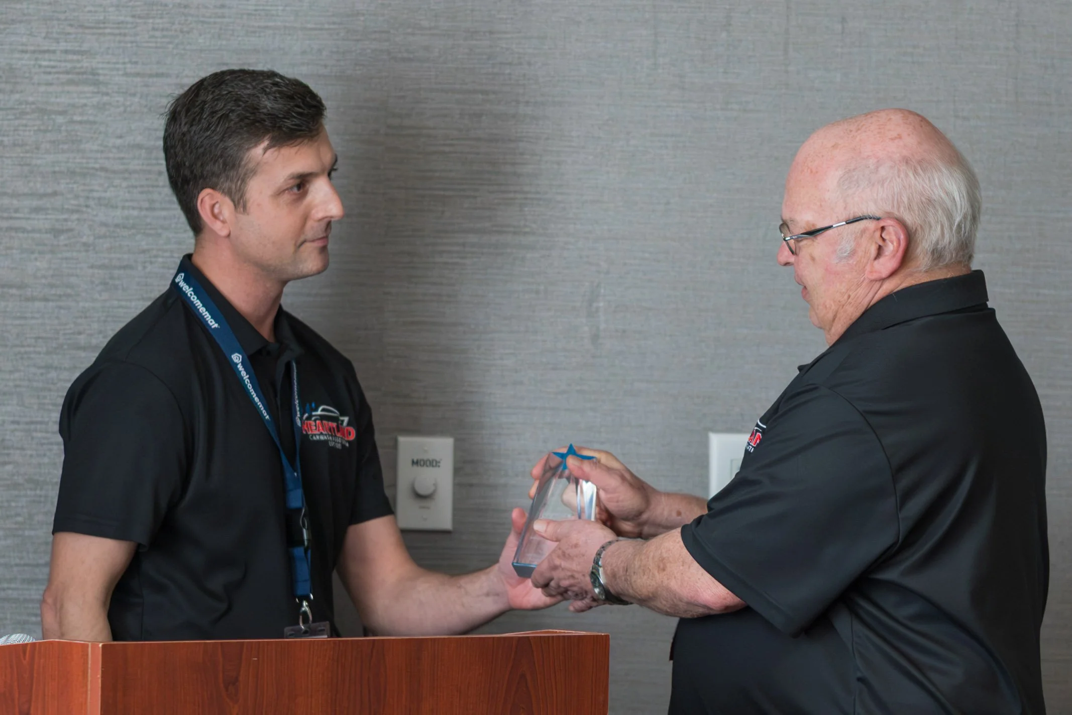 Two men in uniform are standing in front of a gray wall, with one man handing an award or gift to the other.