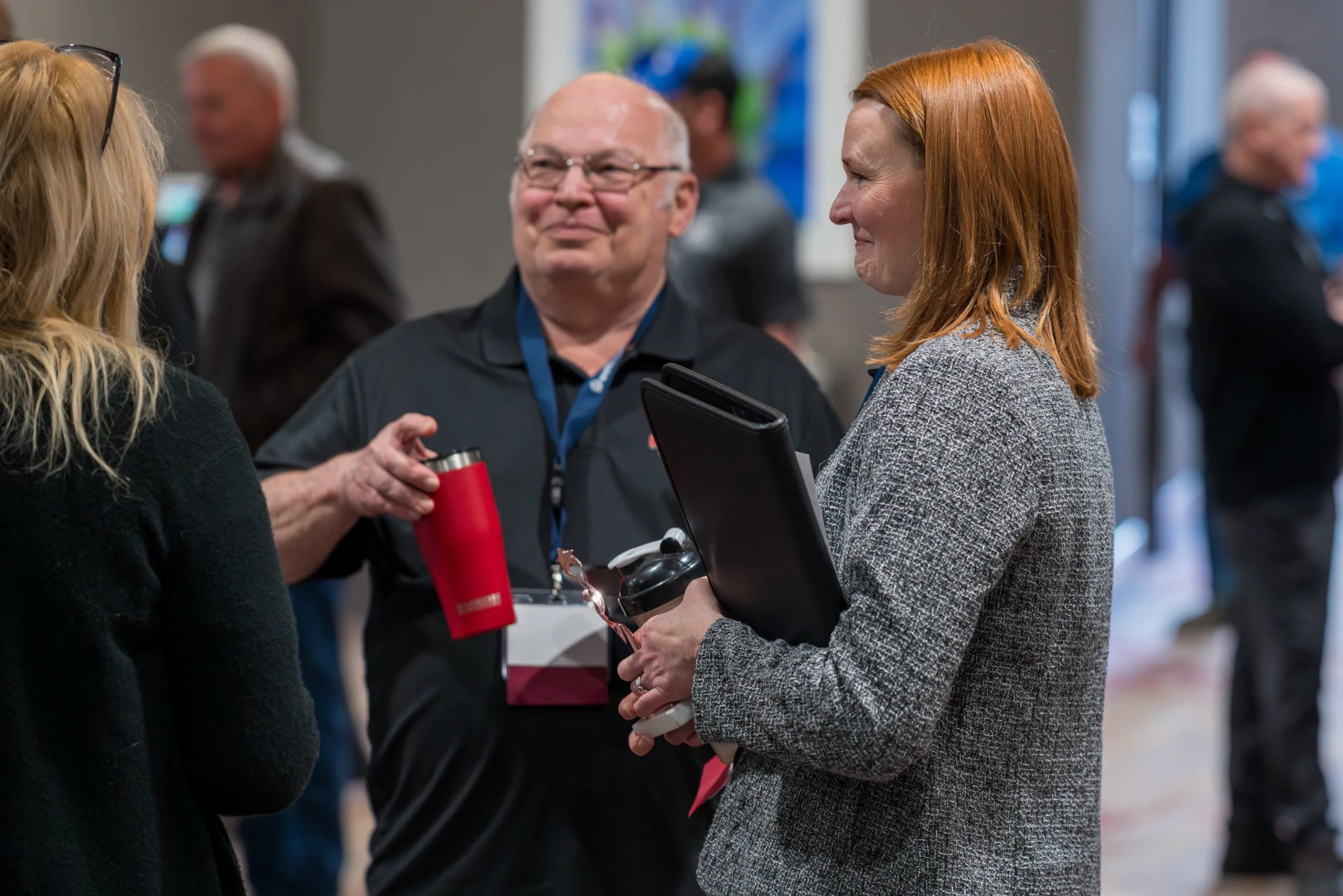 Three people engaged in conversation at an indoor event, with a blurred background of other attendees.