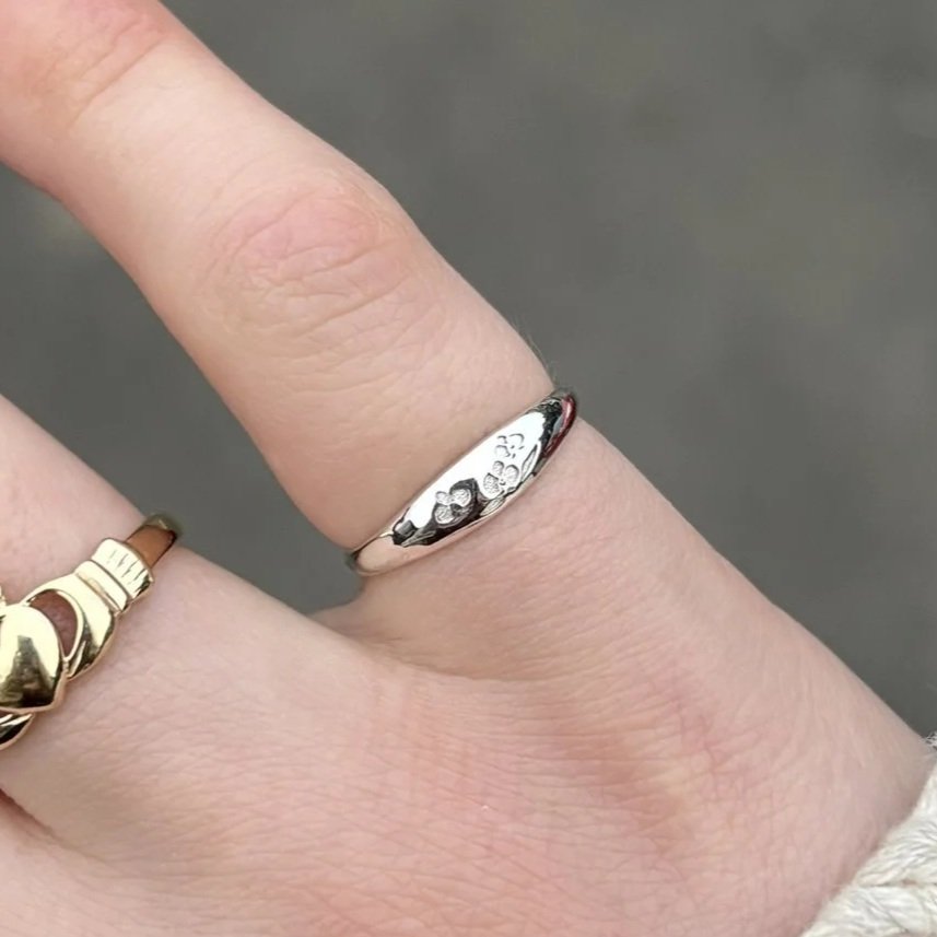Close-up of a hand with two rings on fingers, one silver with floral engravings and one gold with a unique design.