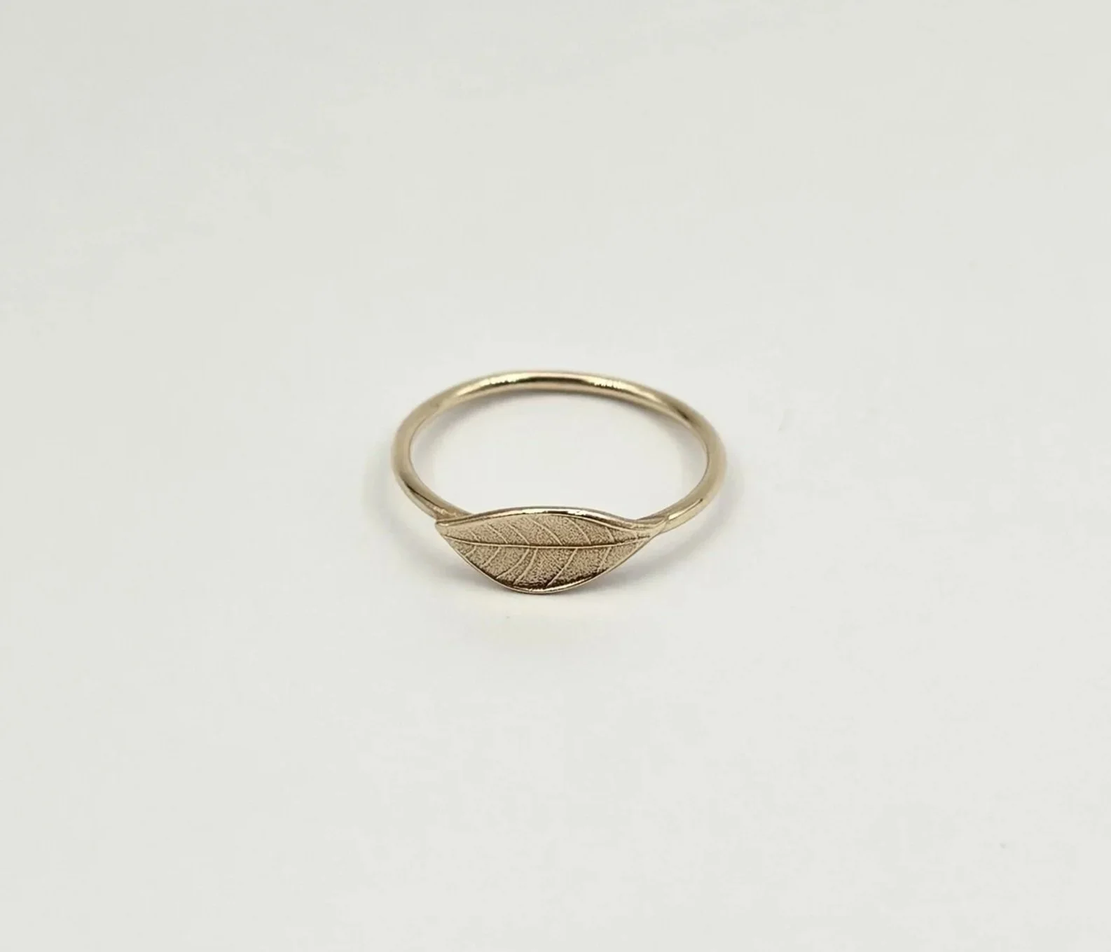 Gold ring with a leaf-shaped design on a plain white background.