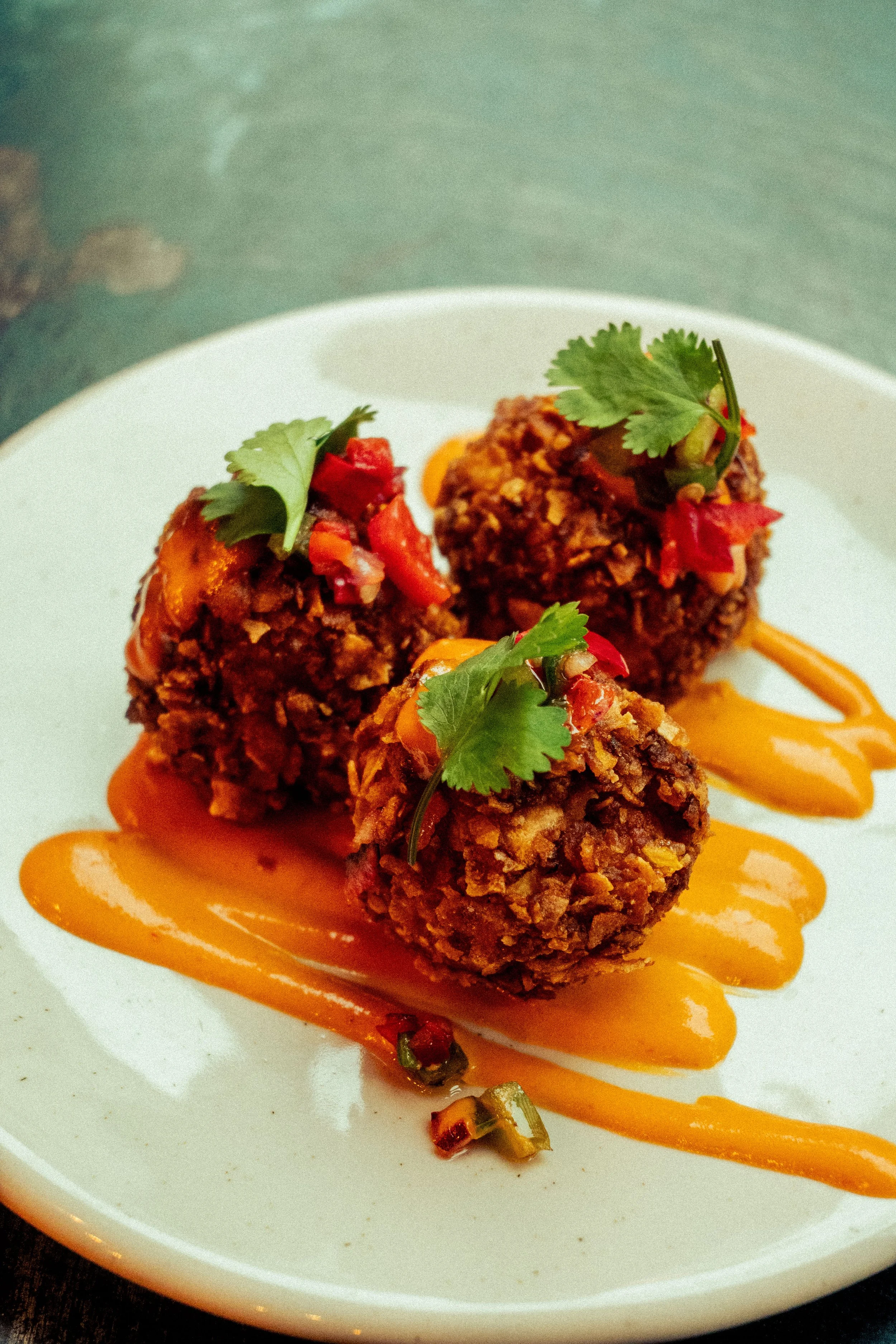Boulettes de banane plantain épicée et panée, servies avec une sauce mayonnaise au piment végétarien sur une assiette blanche.