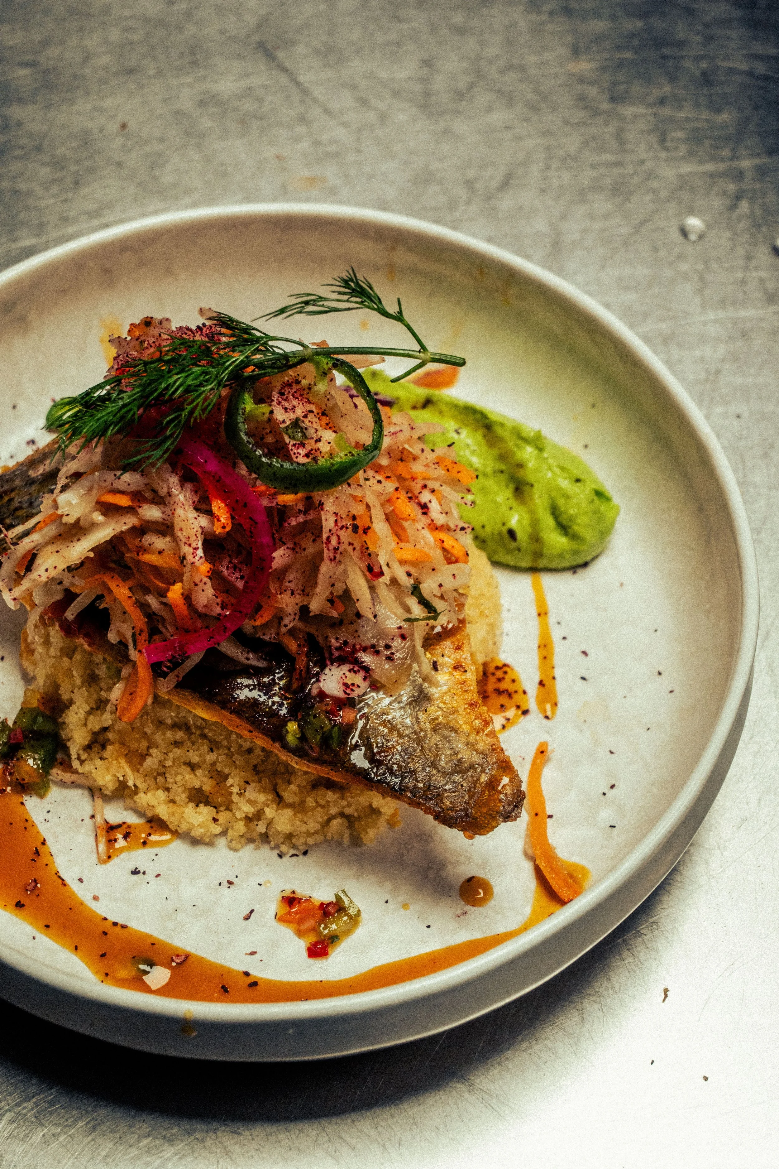 Plat d'attiéké poisson - semoule de manioc et poisson grillé accompagné de légumes, coulis de passion, sauce verte et garnitures délicates.