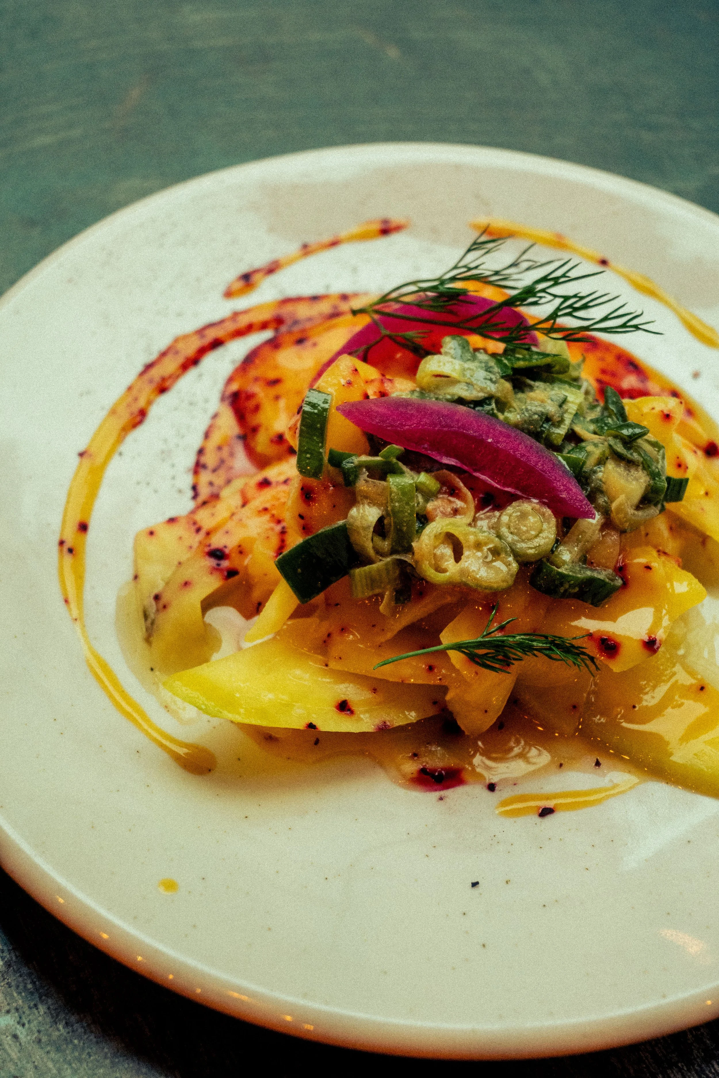 Assiette de mangues marinées avec sauces et garnitures colorées, décorée de fines herbes.
