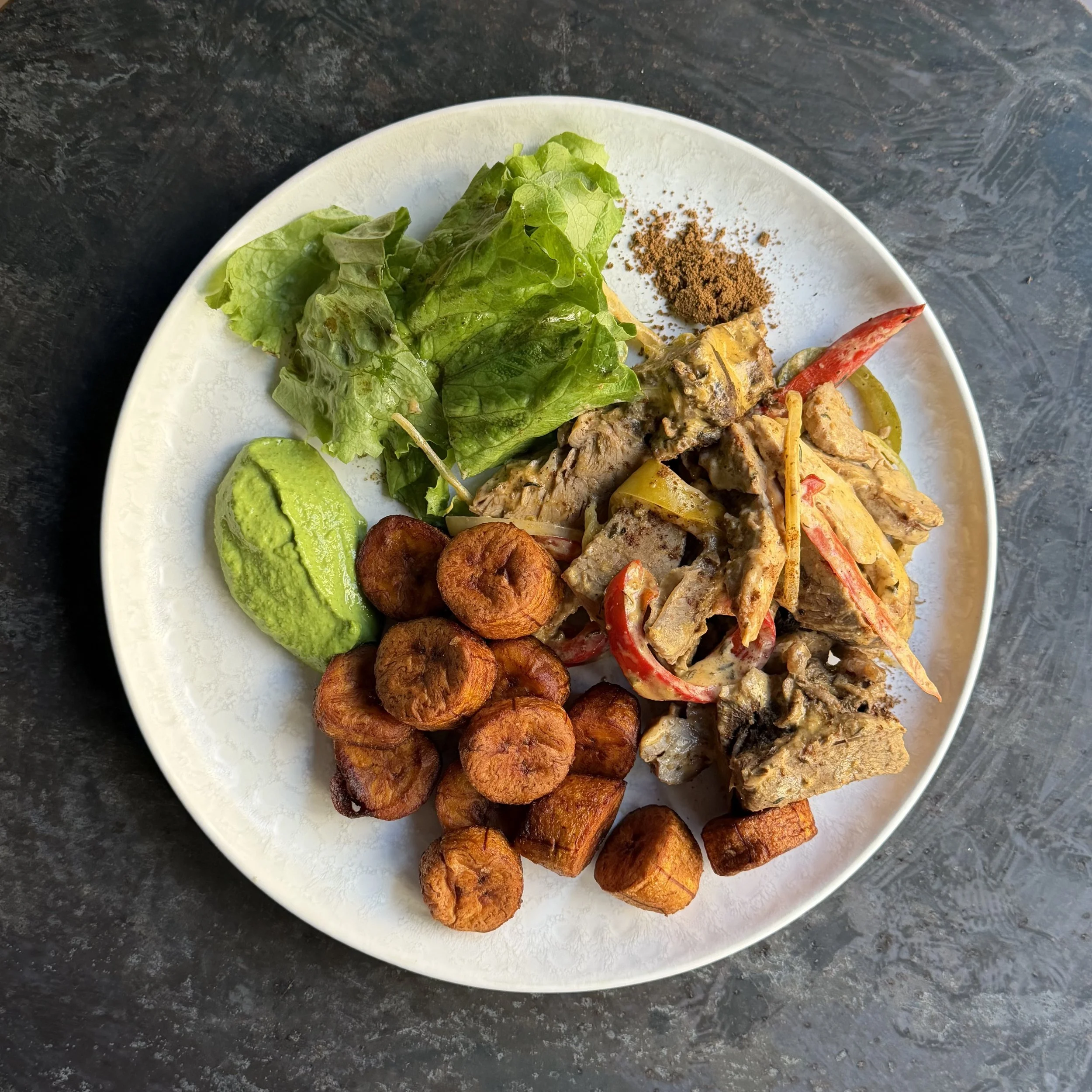 Assiette avec du poulet mariné cuit à l'étouffée avec mayonnaise au piment végétarien, des plantains frits, une salade verte, des poivrons, et du piment en poudre